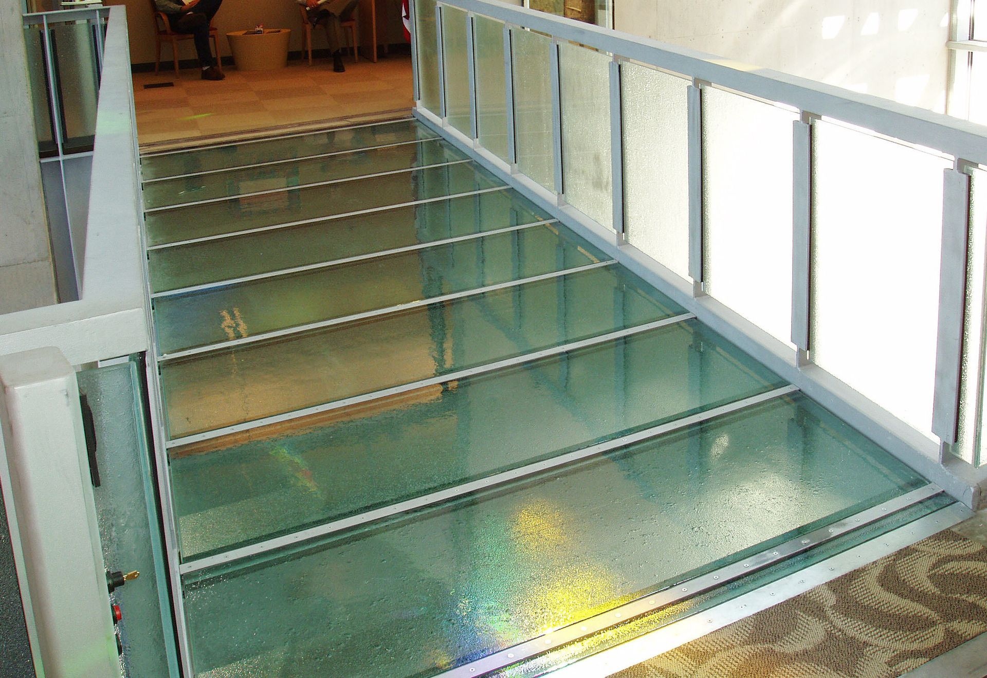 Glass walkway with white railing, sunlight reflection, interior.