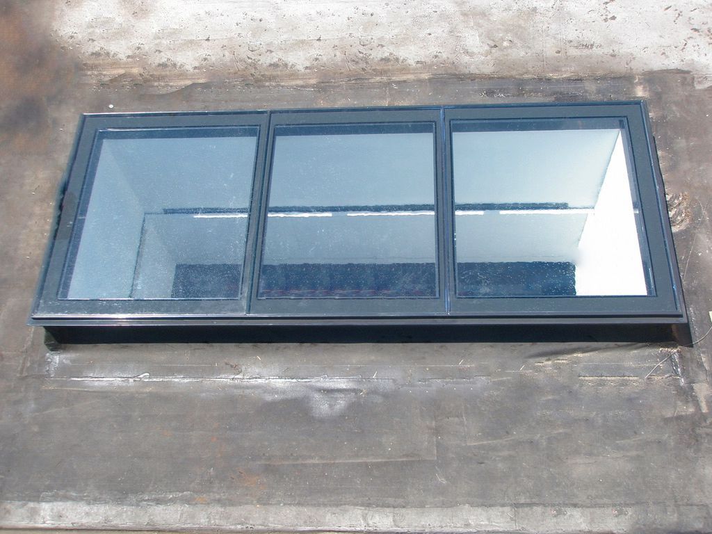 Skylight on a flat roof, with three glass panes in a dark frame.