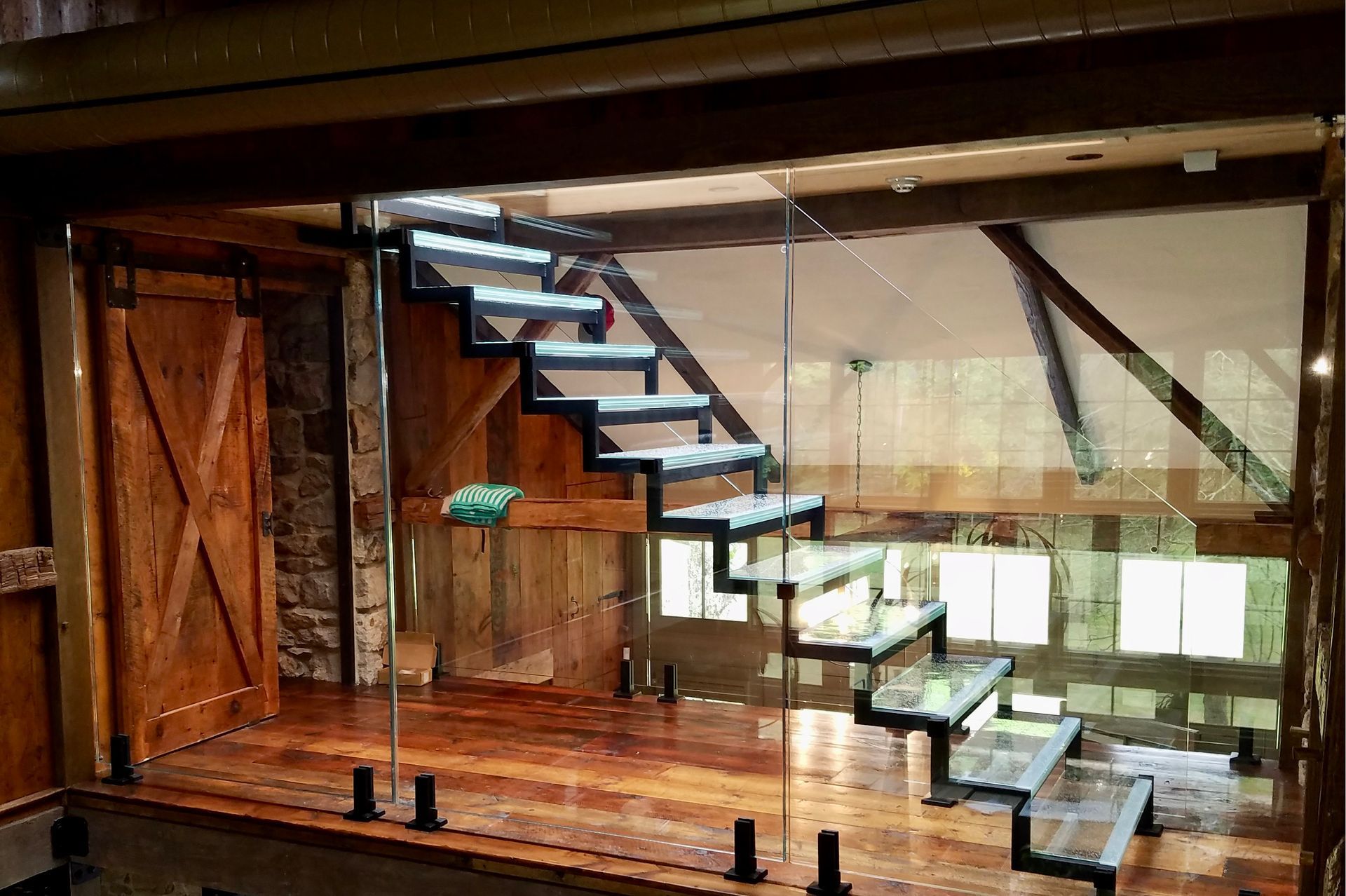 Floating glass and steel staircase in a wooden interior with an open window.