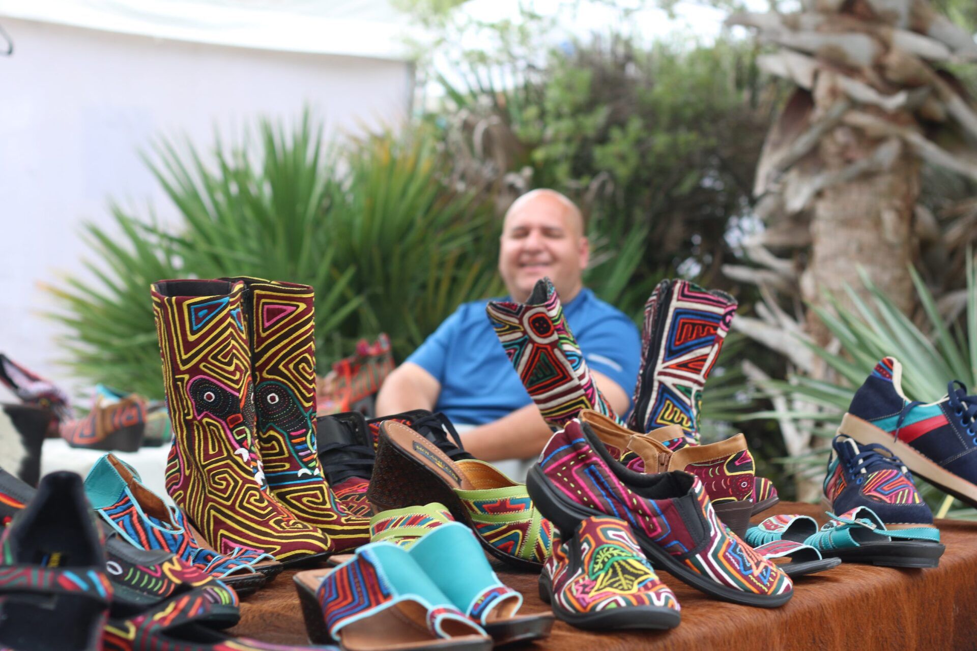 Man behind a table selling colorful, patterned shoes outdoors.