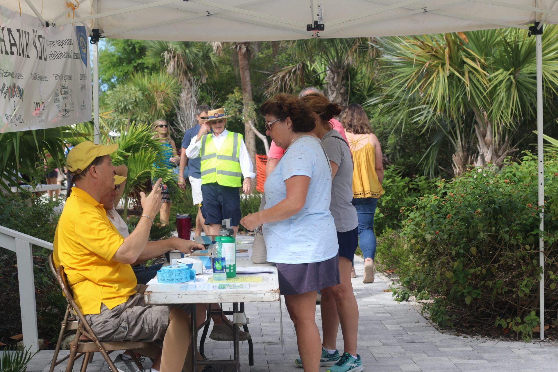 People at an outdoor event registration table; man in yellow shirt, others waiting in line.