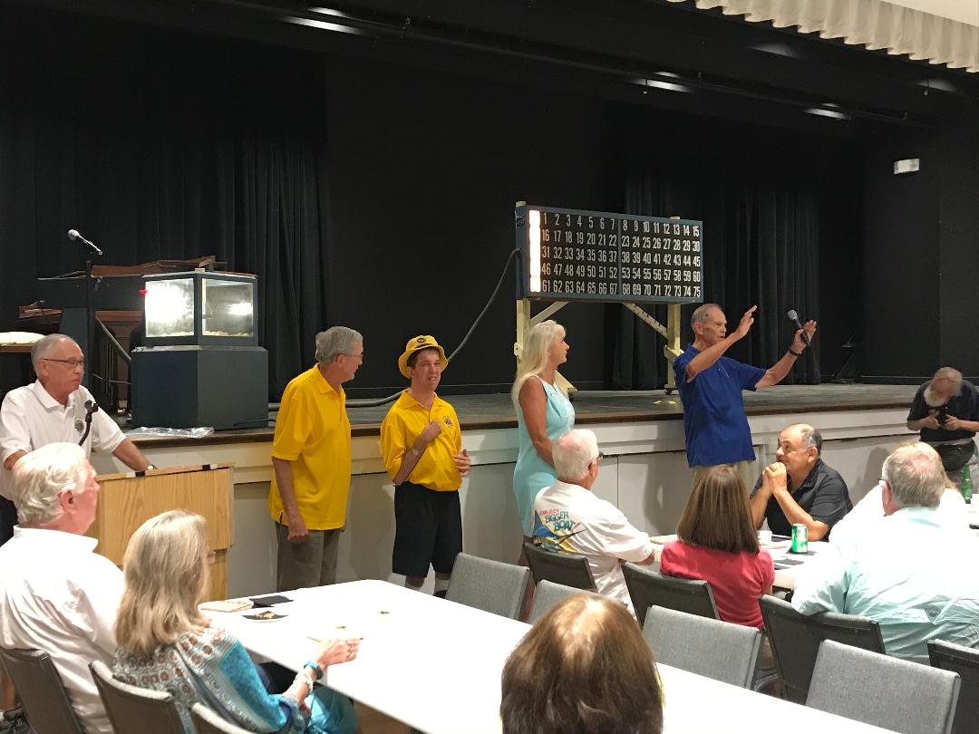 People at a bingo game: stage with players, caller, score board, and table seating.