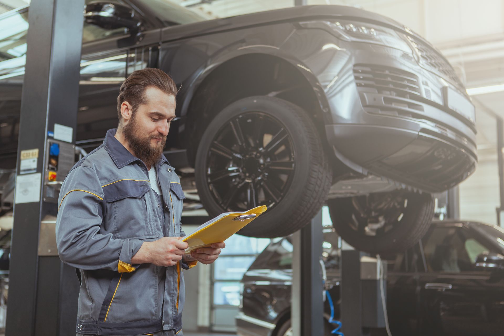 A mechanic is looking at a clipboard in front of a car on a lift  | Weldon’s Auto Center