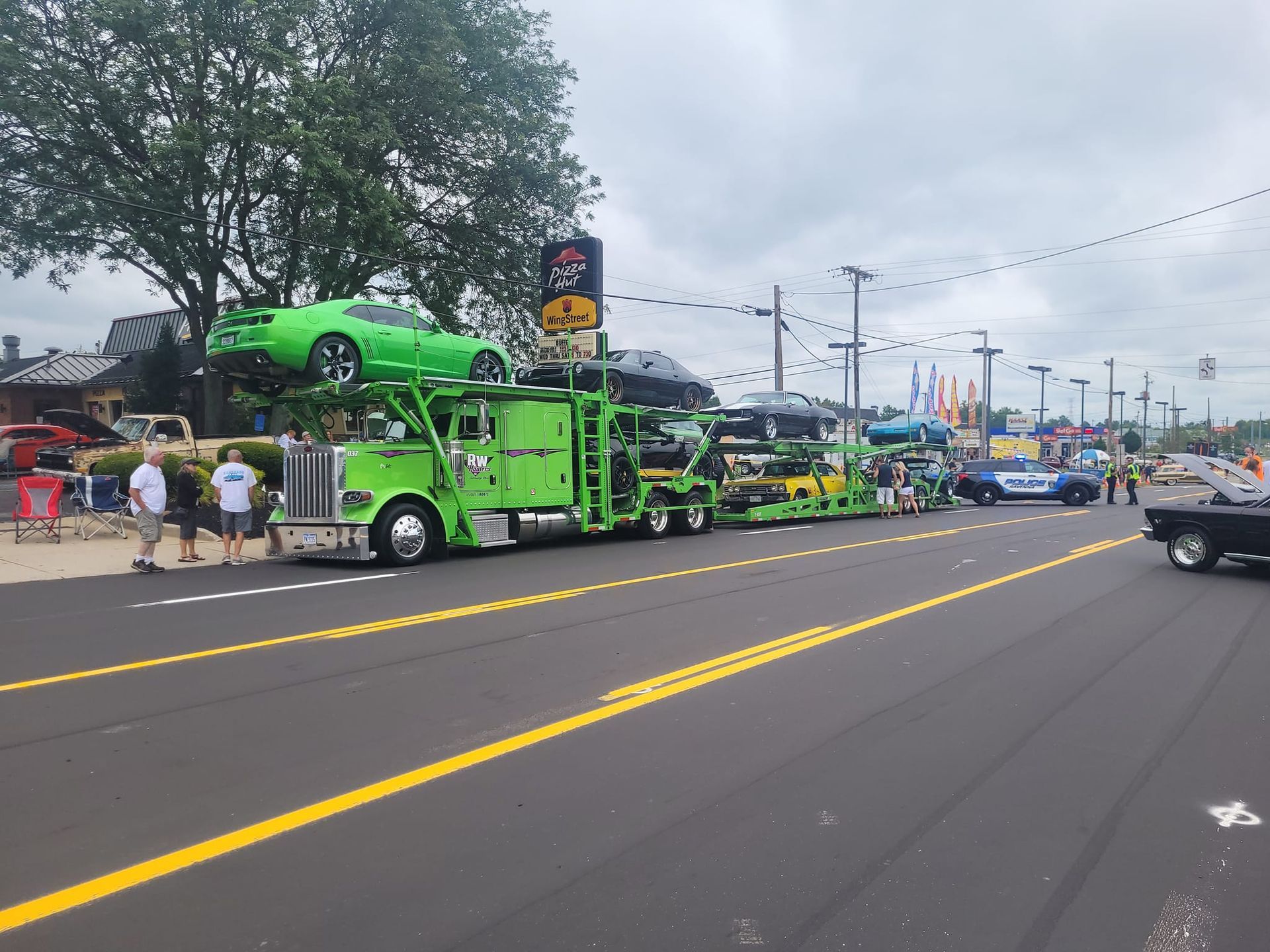 RW Hauler truck carrying sports cars down a parade street