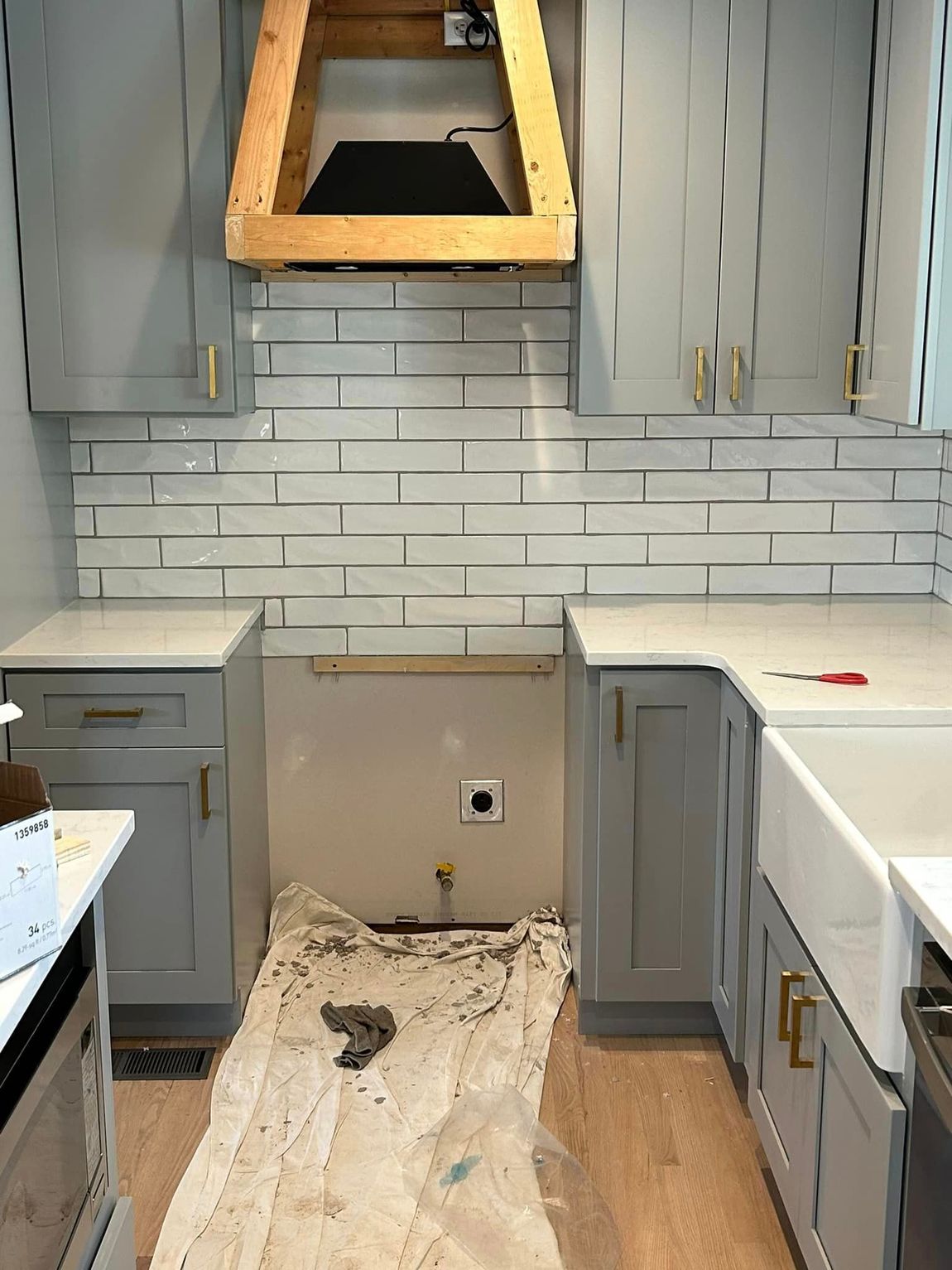 a kitchen with gray cabinets , white counter tops , and a wooden hood .