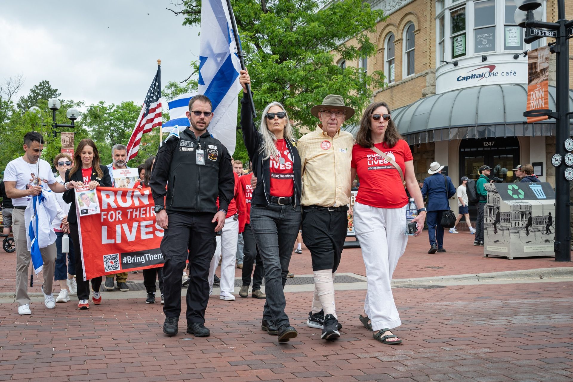 A group of people marching down a brick street, some holding flags and a sign that reads 