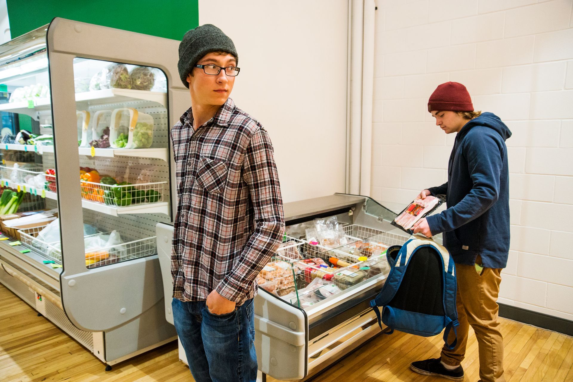 Two men are standing in front of a refrigerator in a grocery store.