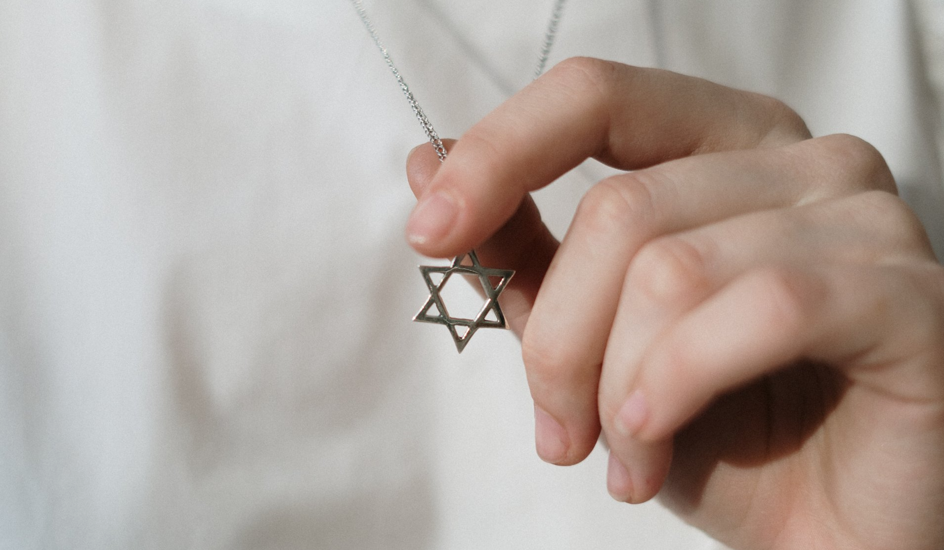 A person is holding a necklace with a star of david pendant.