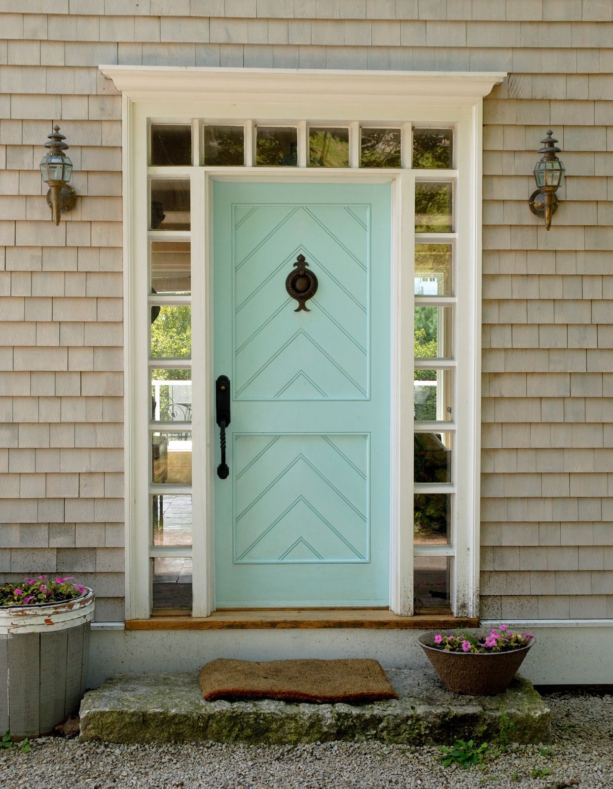 Aqua-painted door with chevron design and glass sidelights; framed by a white trim, stone steps, and wall-mounted lights.