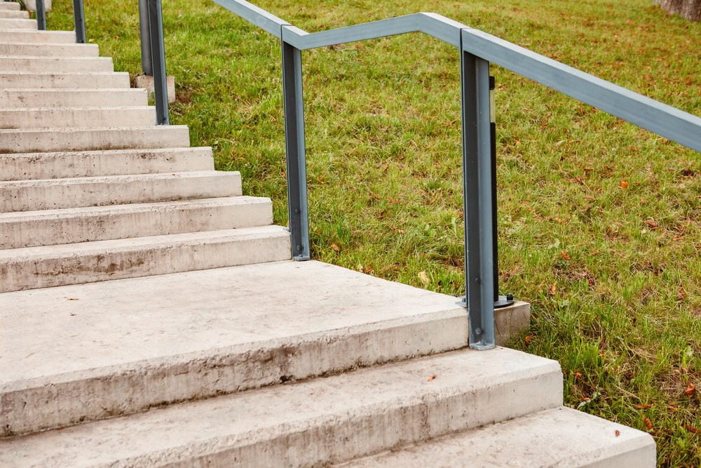 A row of concrete stairs with a metal railing going up a grassy hill.