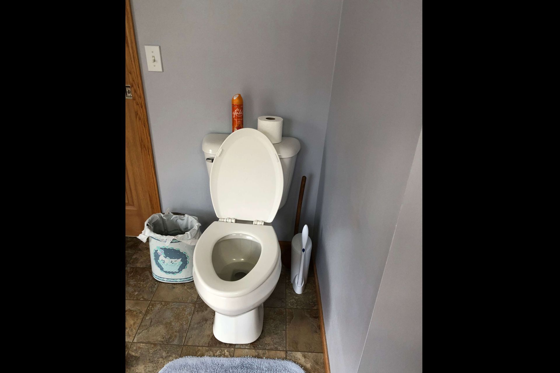 A toilet is sitting in a bathroom next to a trash can.