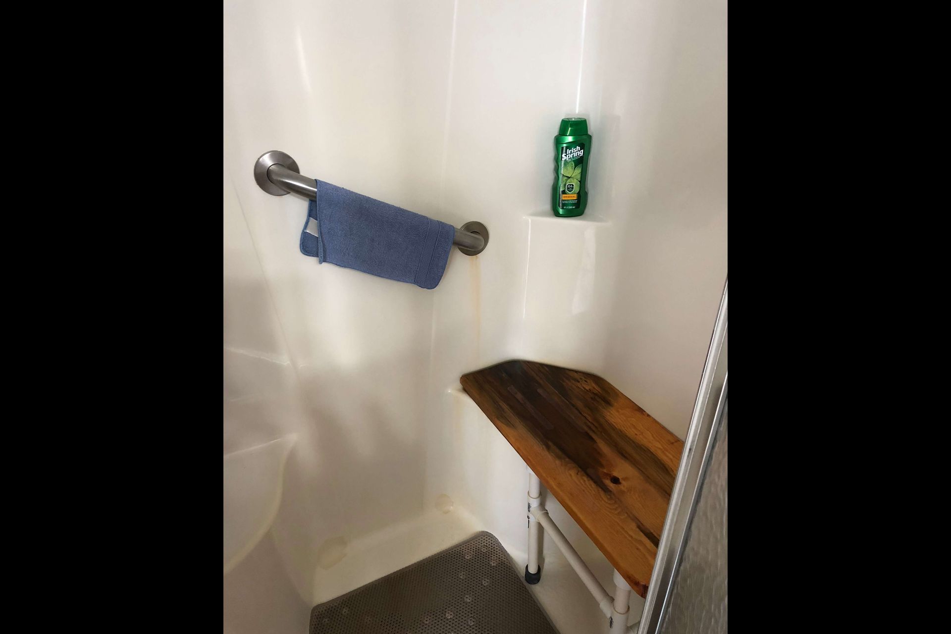 A shower with a wooden bench and a towel hanging on the wall.