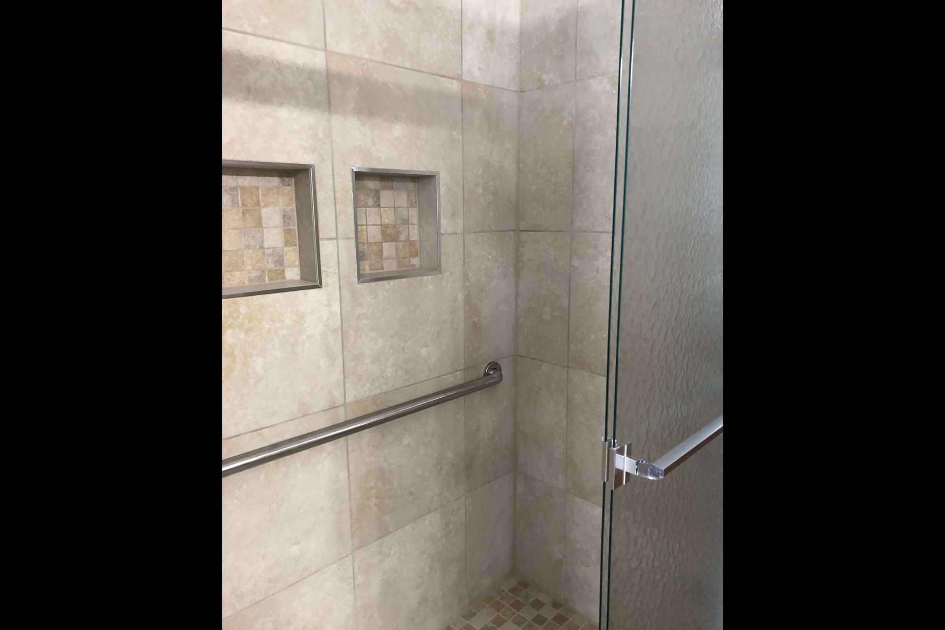 A walk in shower with a glass door and a railing.