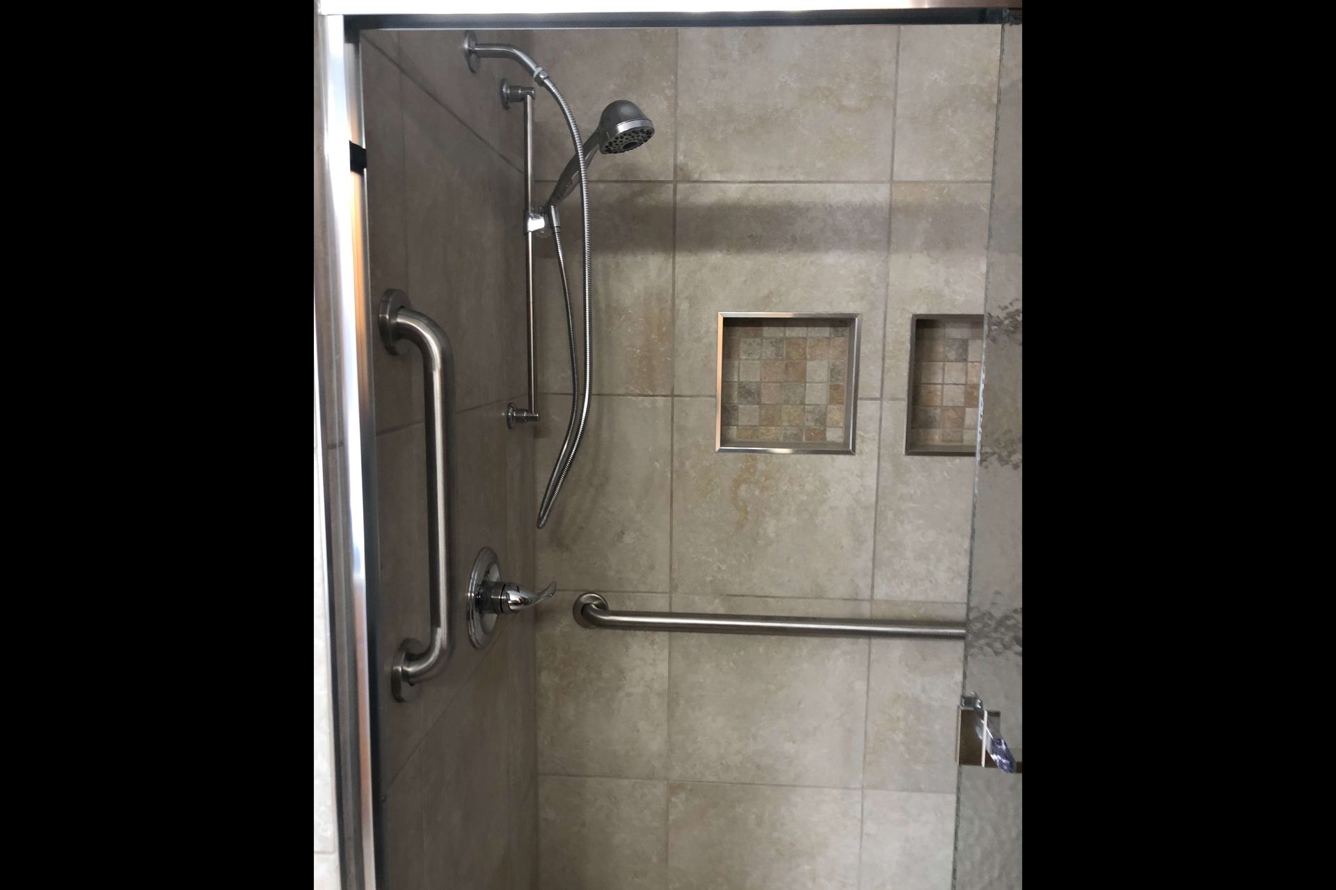 A walk in shower with a glass door and stainless steel handles.