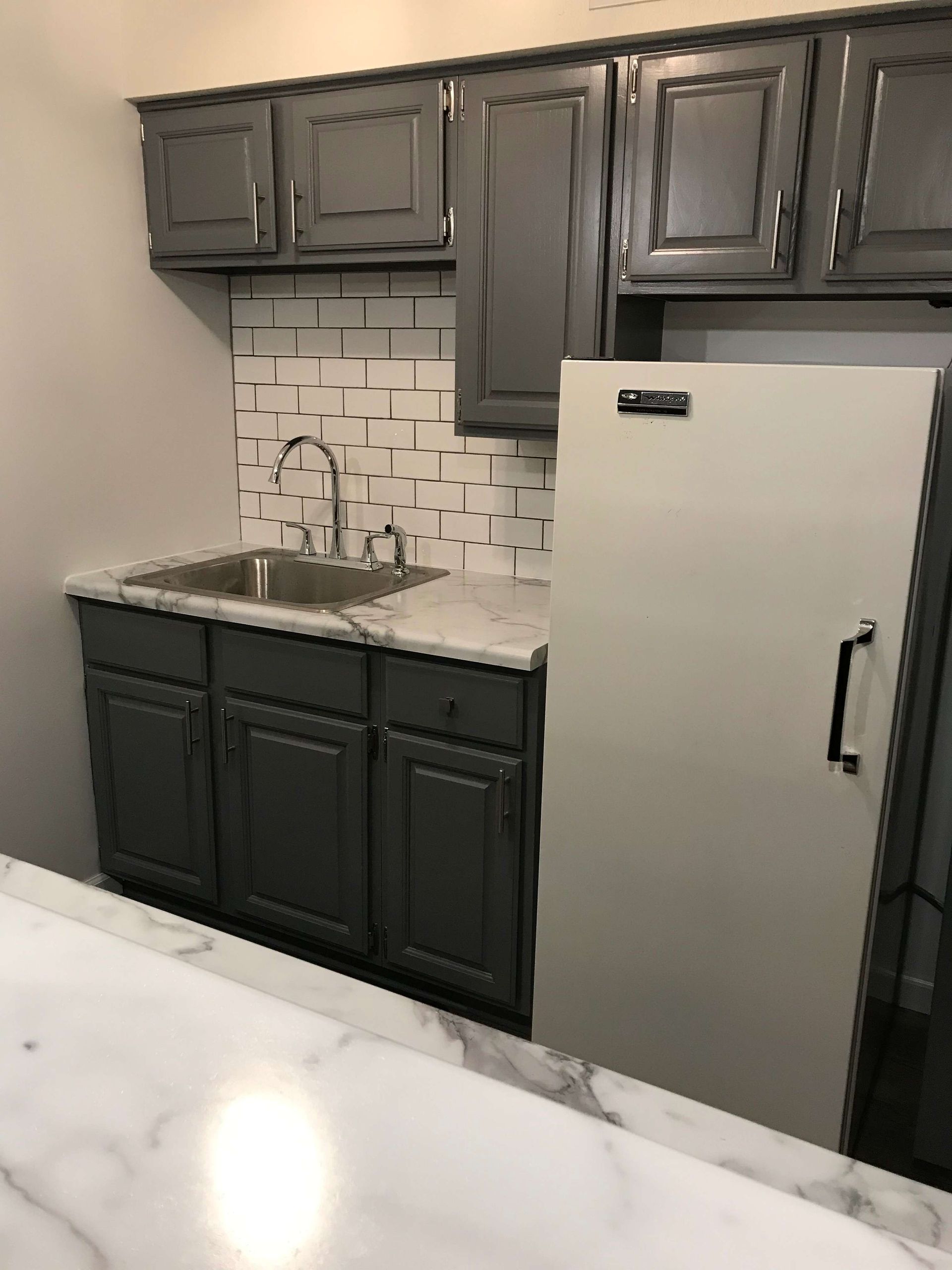 A kitchen with gray cabinets , a sink , and a refrigerator.