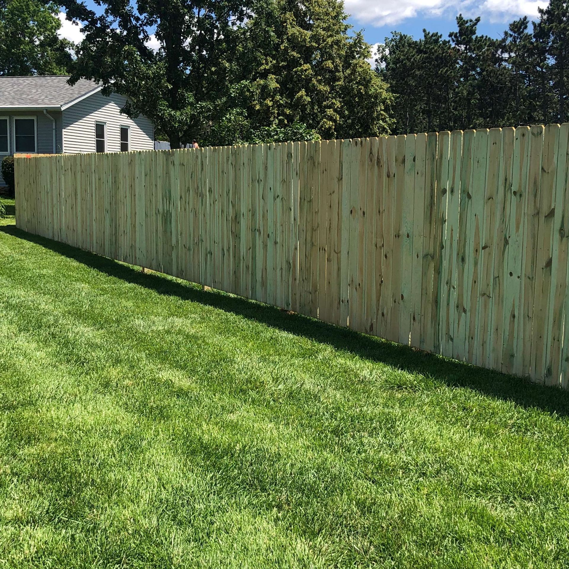 A wooden fence surrounds a lush green lawn in front of a house.