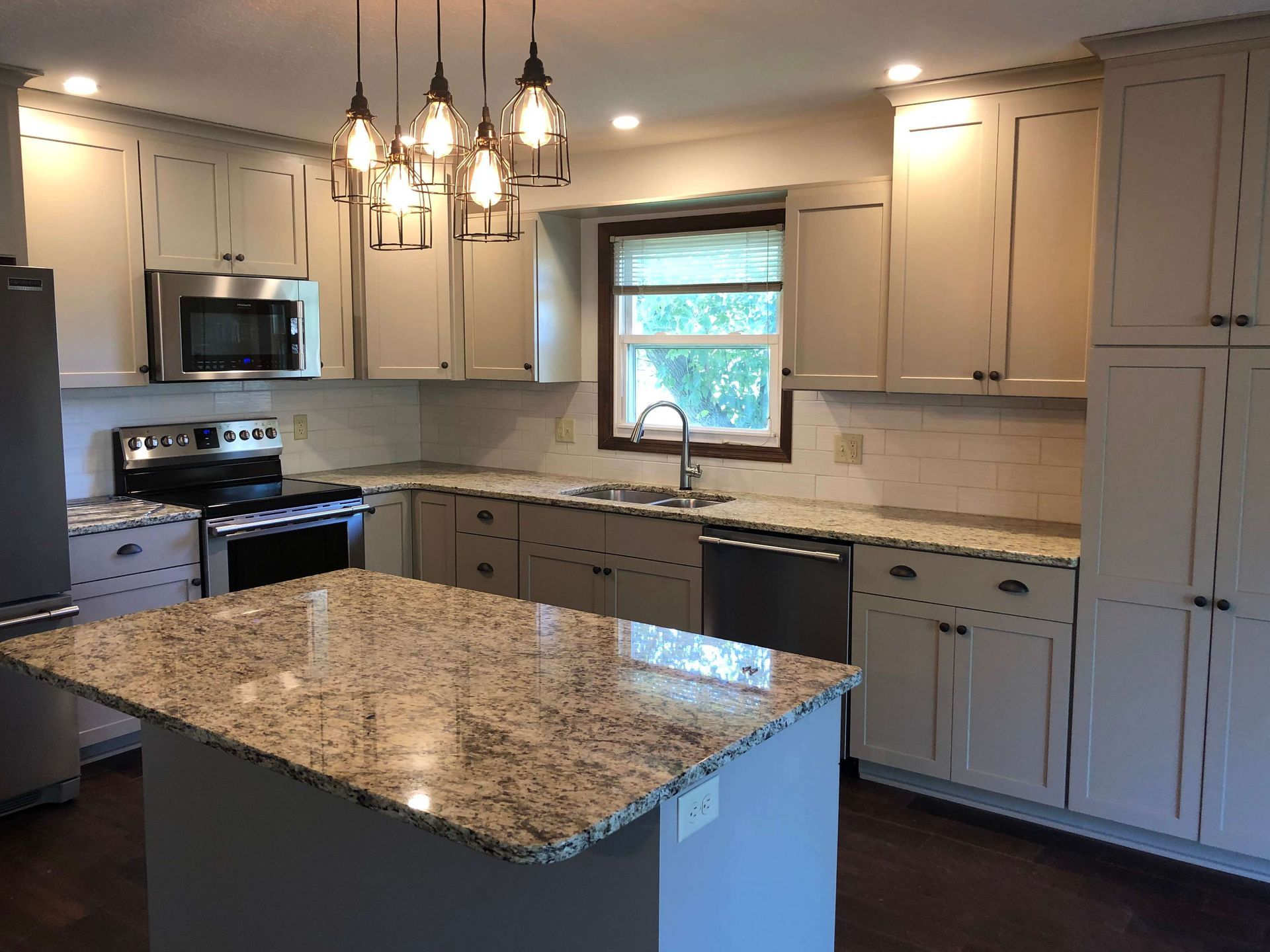 A kitchen with white cabinets , granite counter tops , stainless steel appliances and a large island.