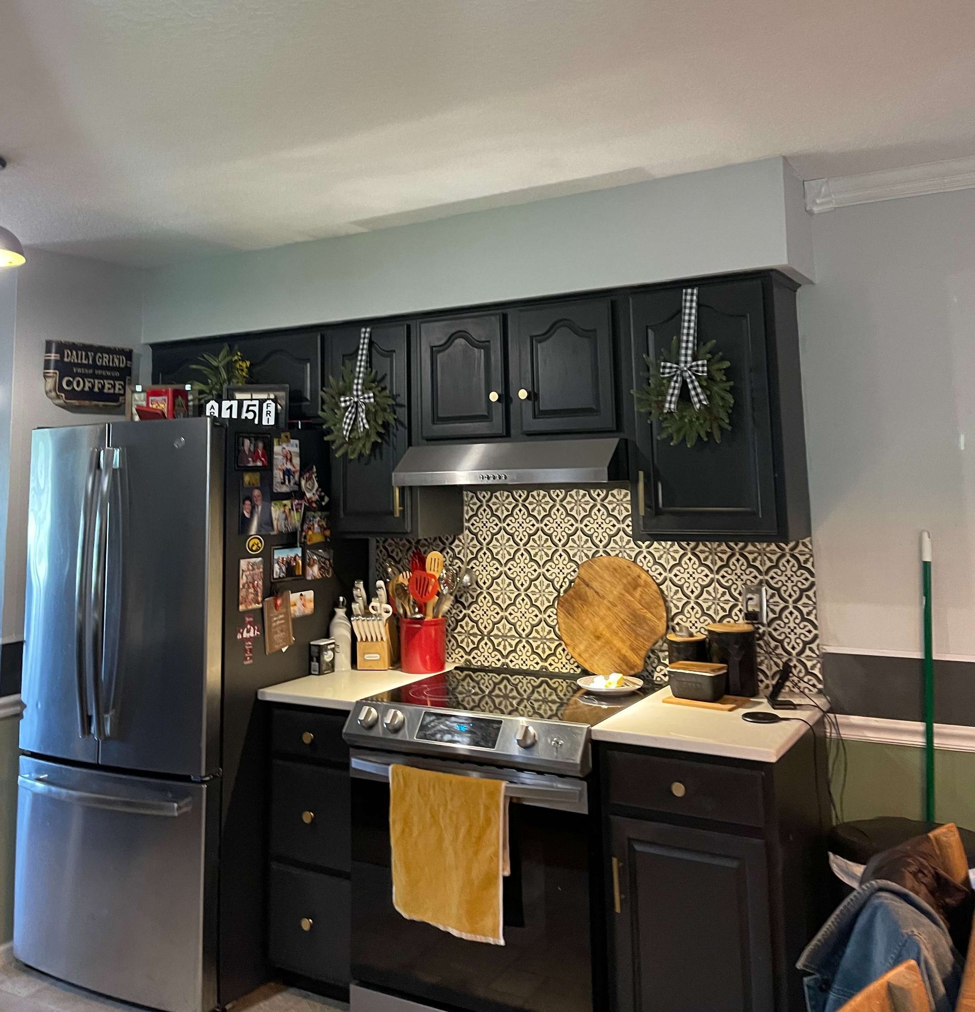 A kitchen with black cabinets and a stainless steel refrigerator