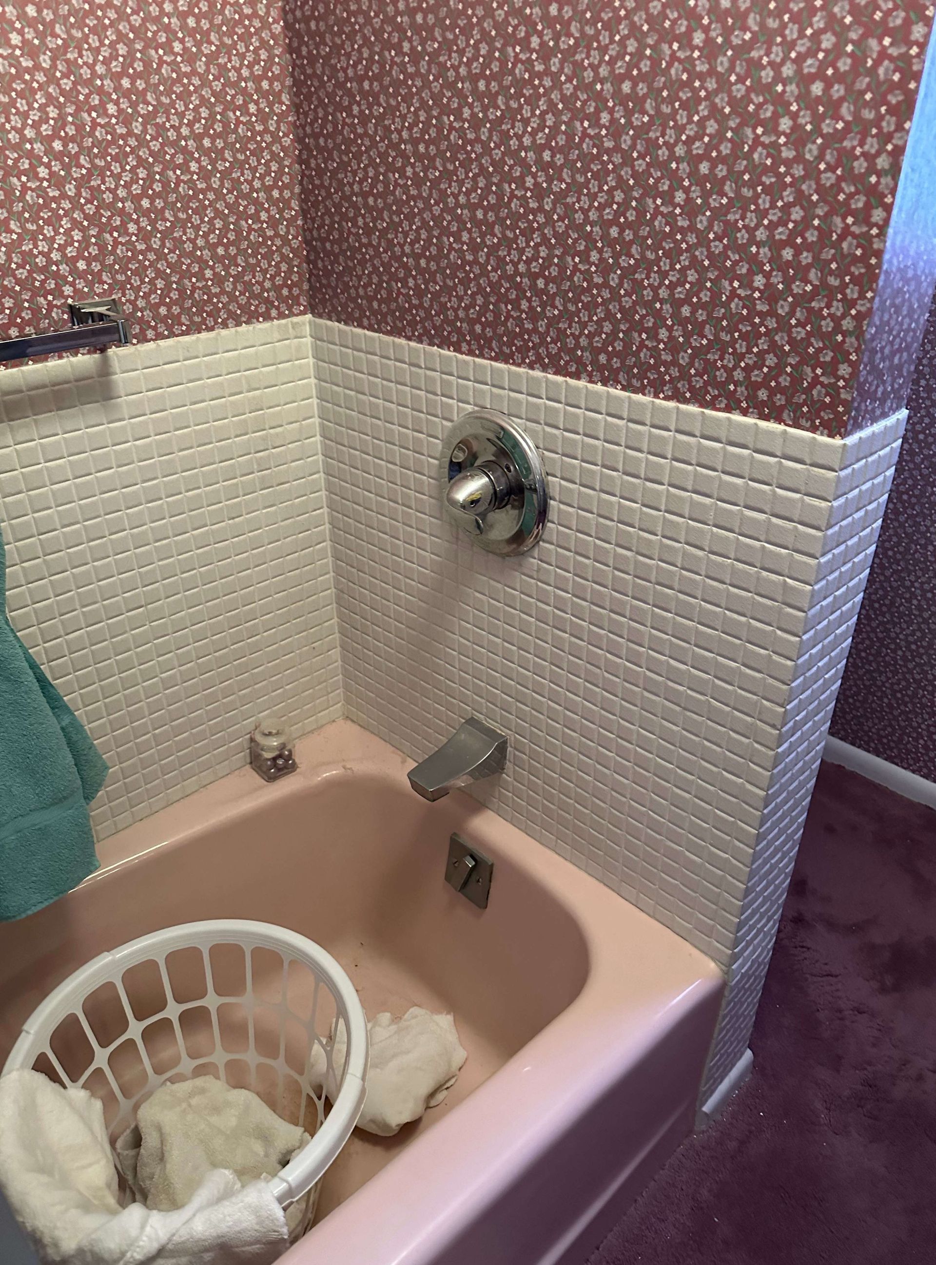 A pink bathtub with a laundry basket in it.