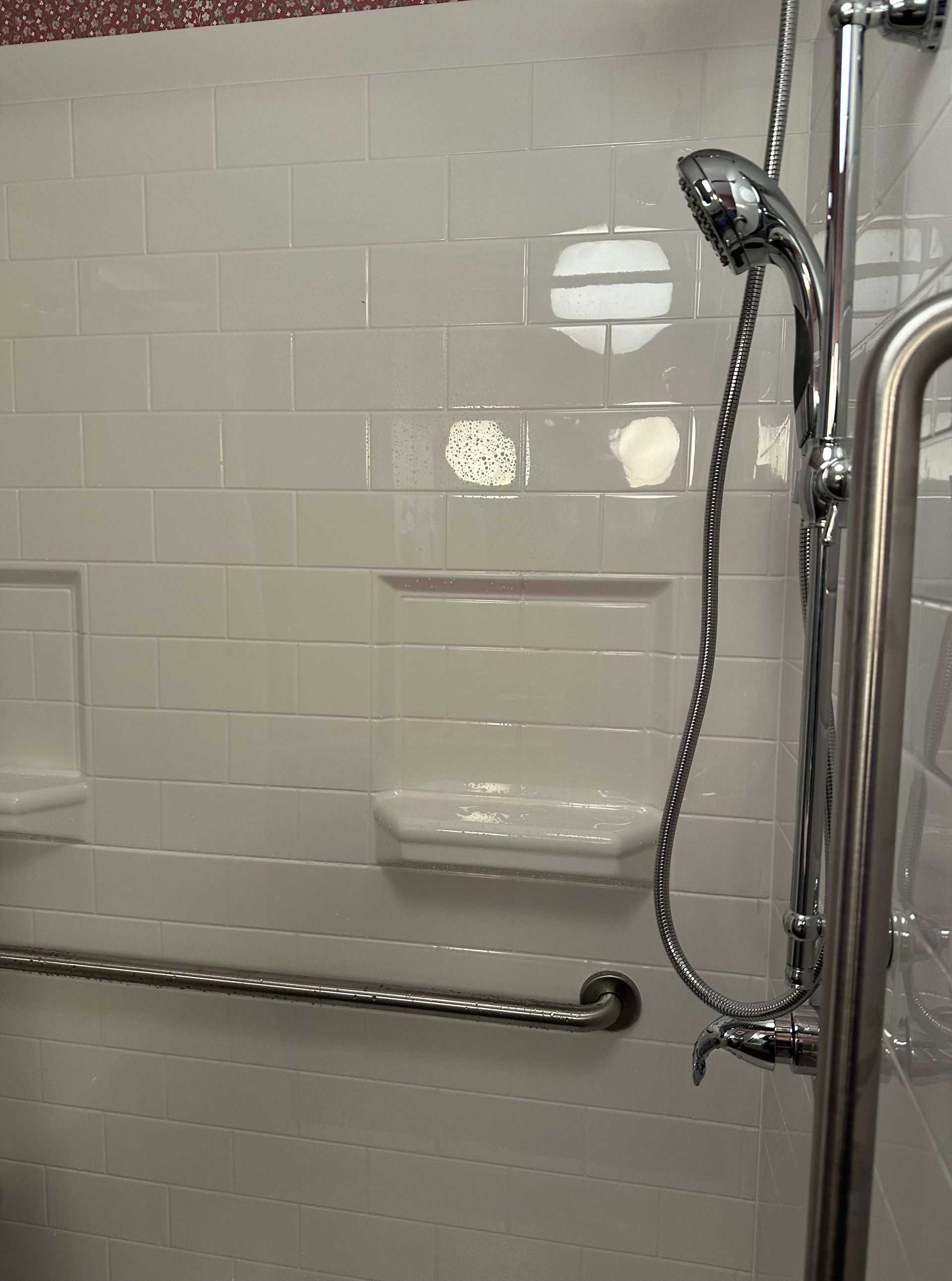 A shower with a hand held shower head and a stainless steel railing.