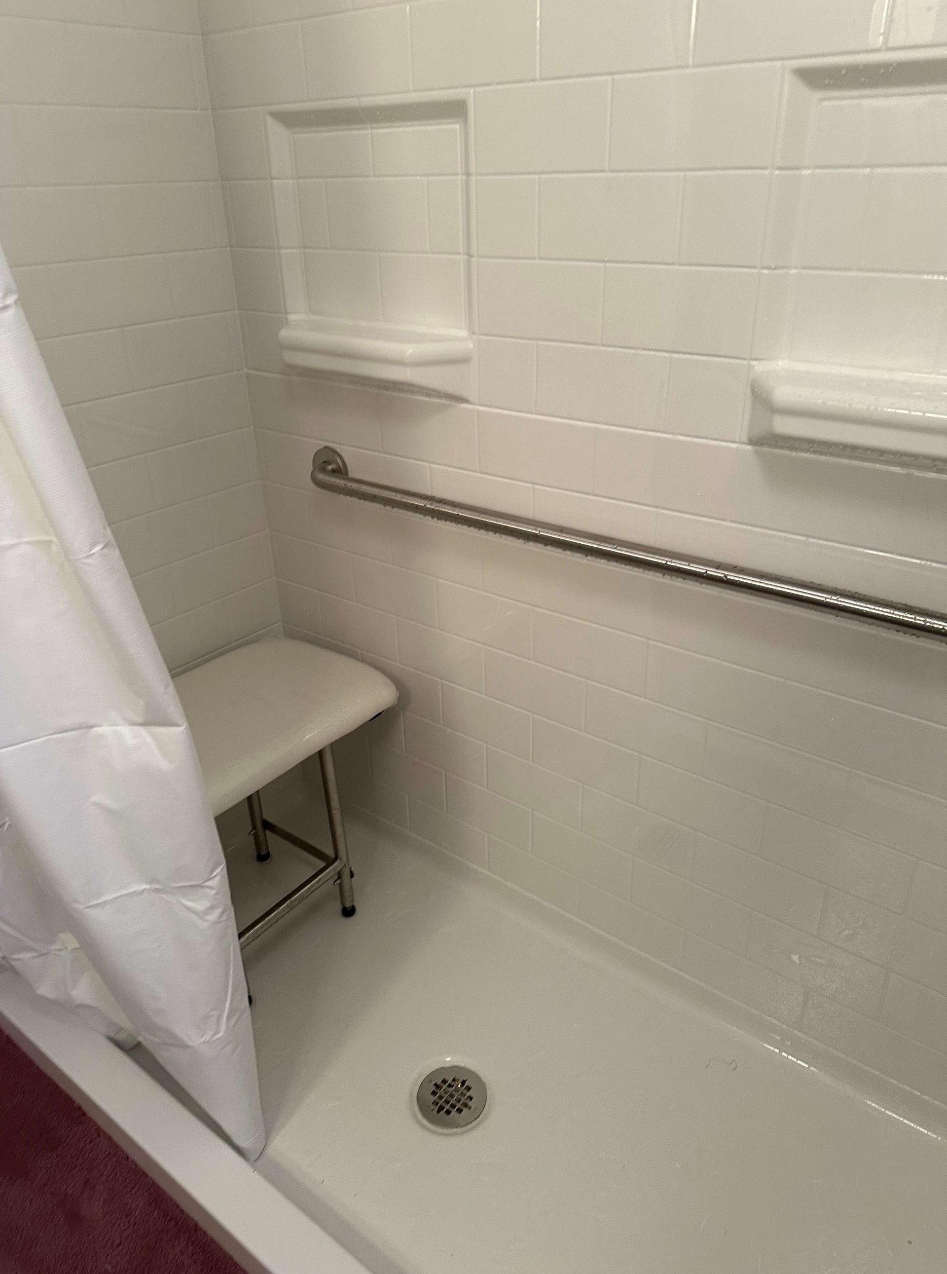 There is a stool in the shower with a railing.