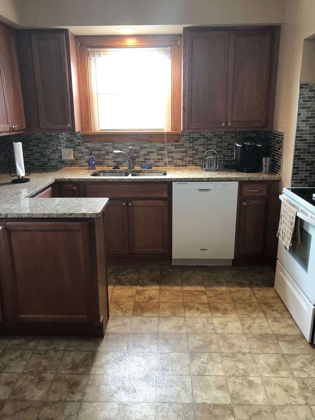 A kitchen with wooden cabinets , granite counter tops , a stove and a dishwasher.