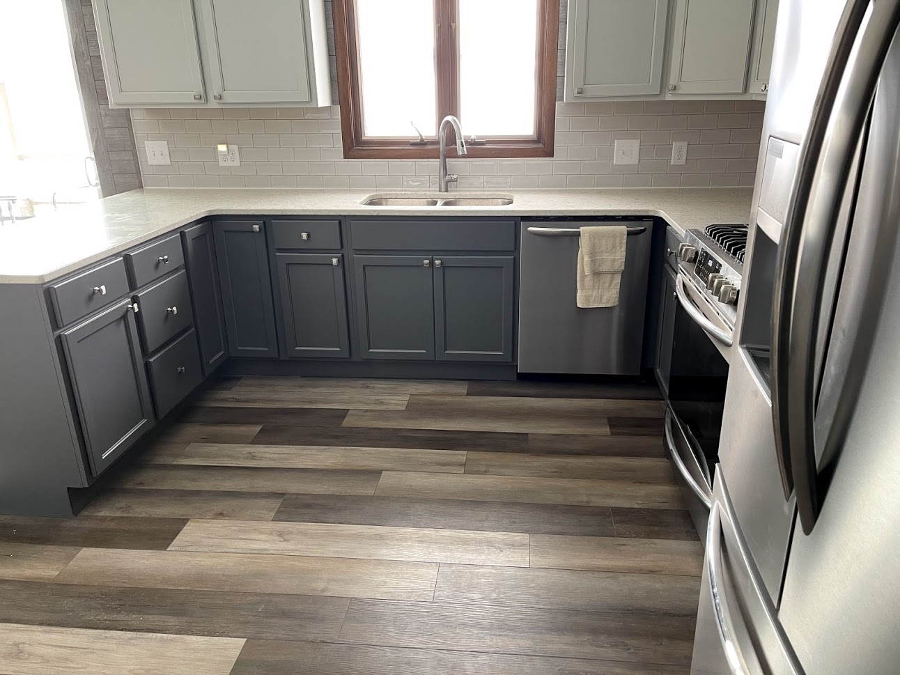 A kitchen with gray cabinets , stainless steel appliances , a sink , and a window.