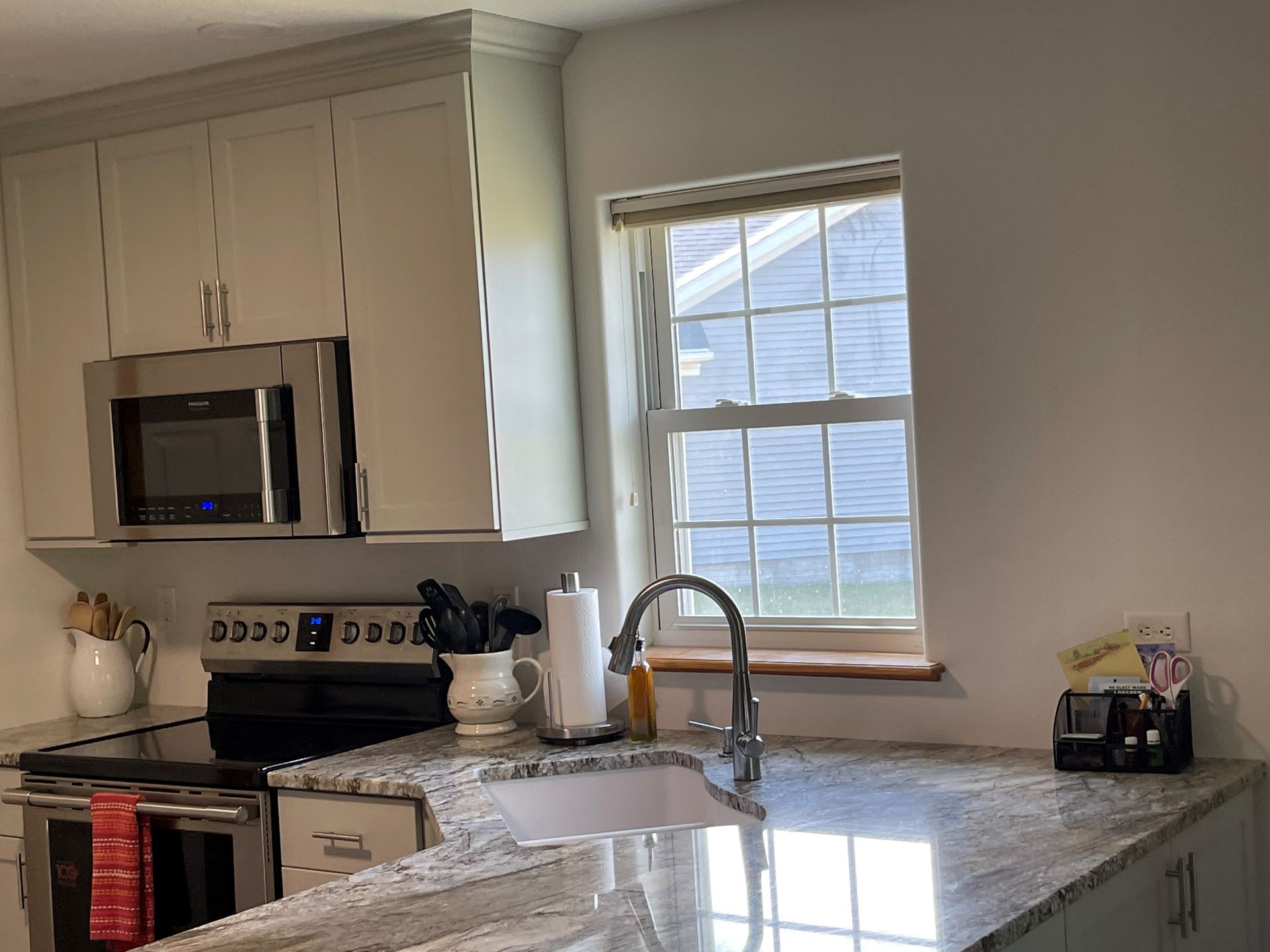 A kitchen with a sink , stove , microwave and window