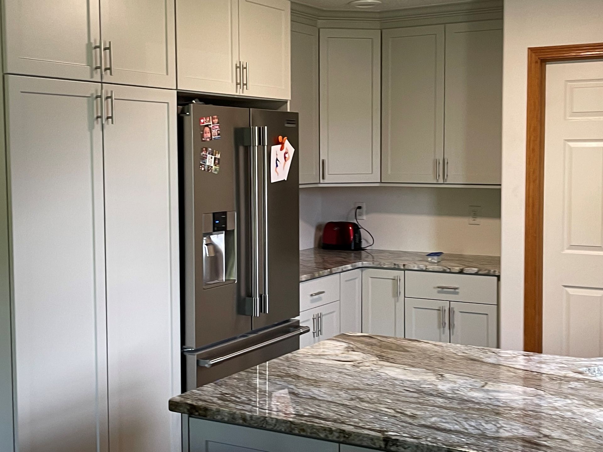 A kitchen with white cabinets , granite counter tops , and a stainless steel refrigerator.