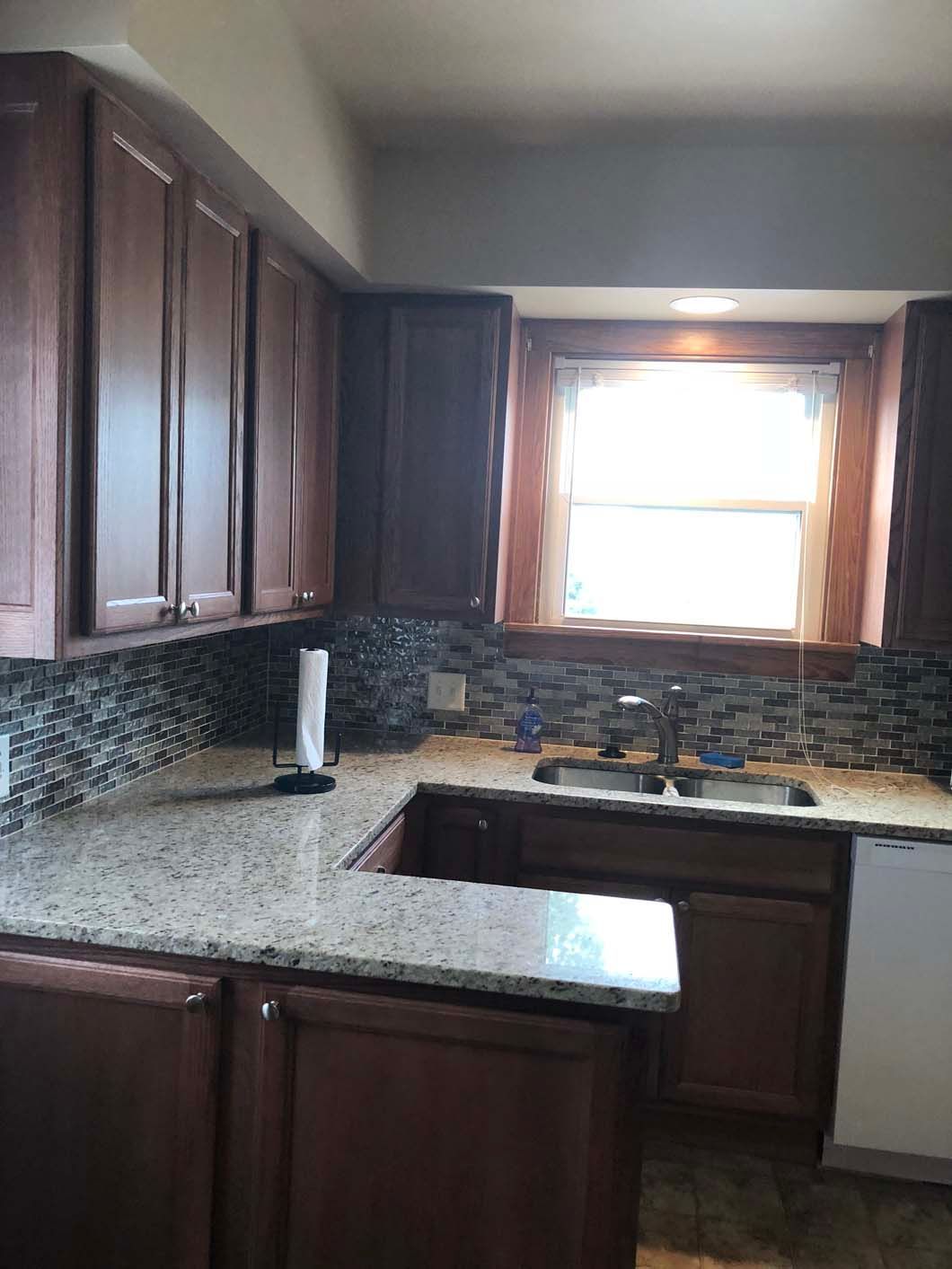 A kitchen with wooden cabinets , granite counter tops , a sink and a window.