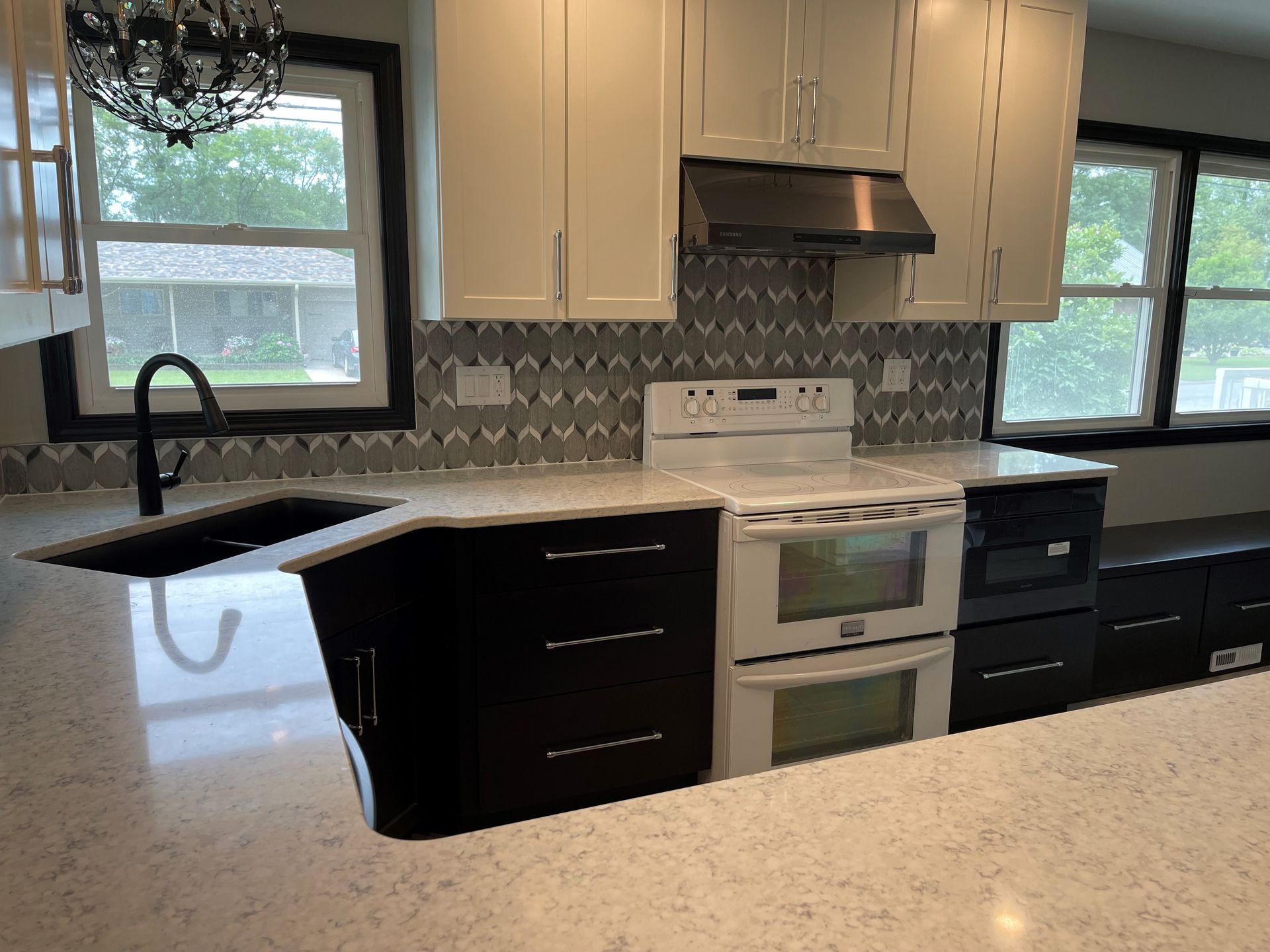 A kitchen with white cabinets , black cabinets , a stove and a sink.