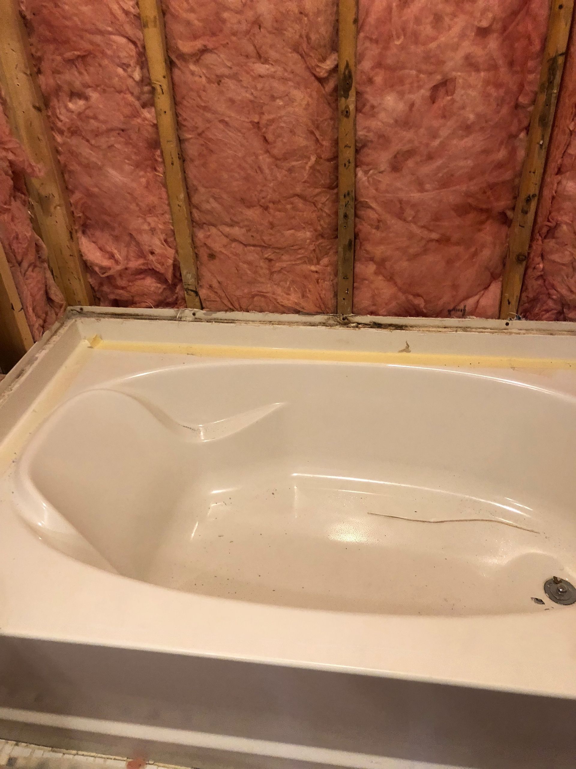 A bathtub is sitting in a room with pink insulation on the walls.