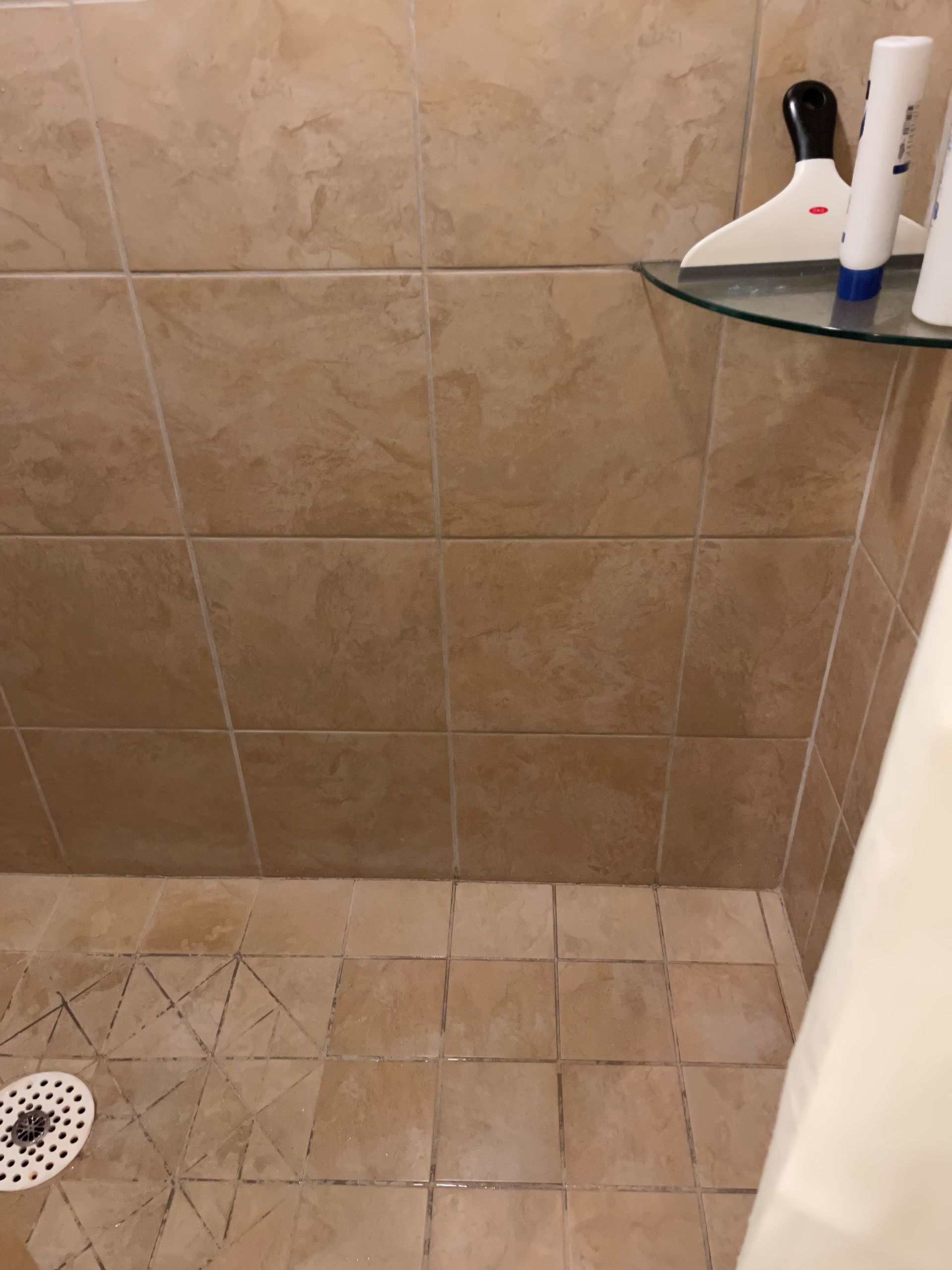 A shower with a drain and a shelf with bottles on it