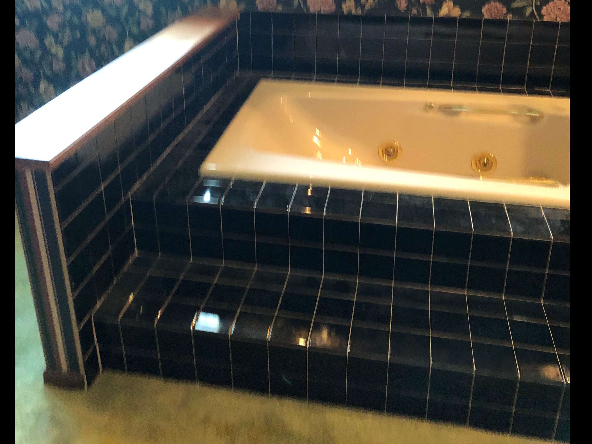A bathtub surrounded by black tiles in a bathroom