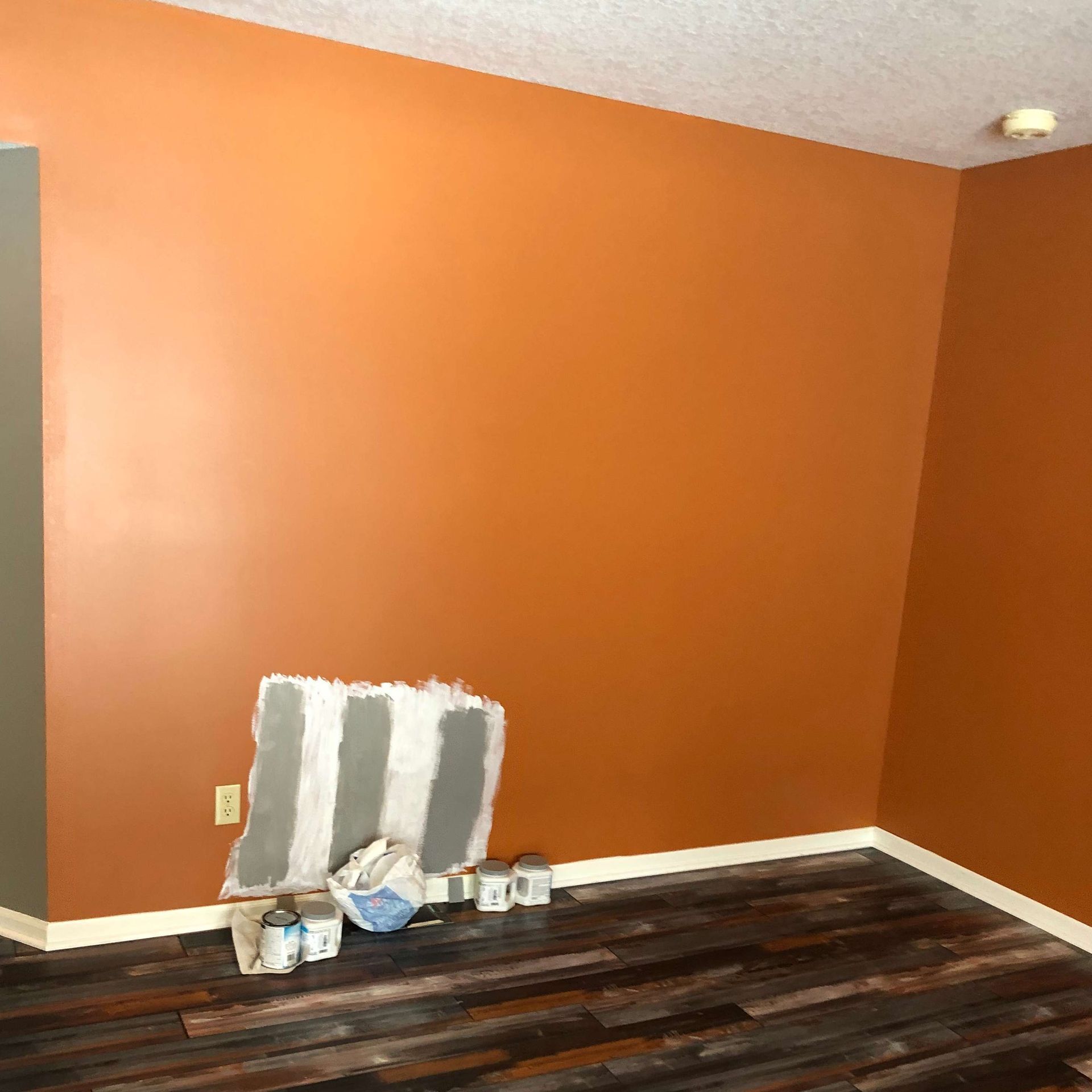 A room with orange walls and wooden floors is being painted.