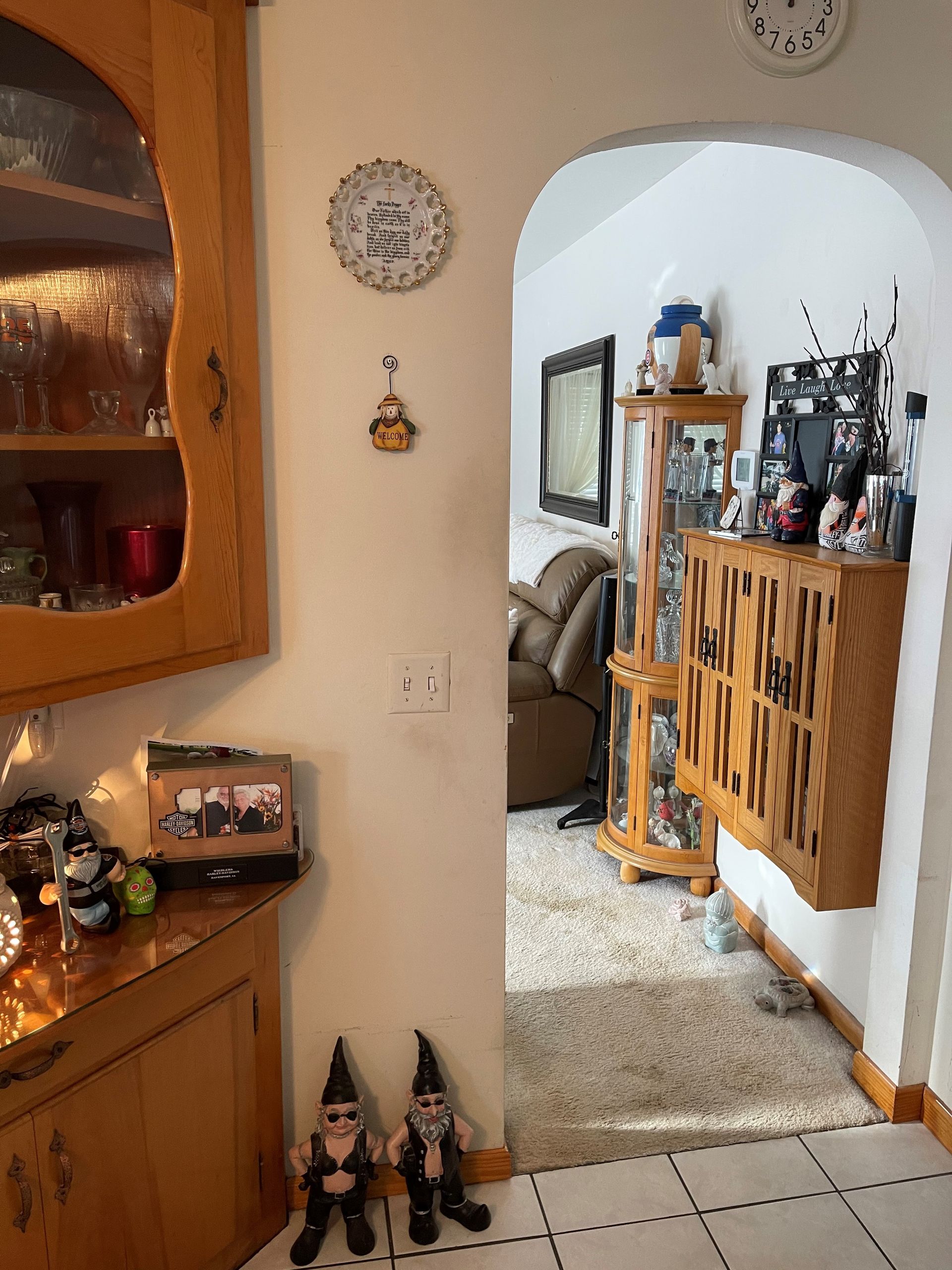 A living room with a clock on the wall and two gnomes on the floor.