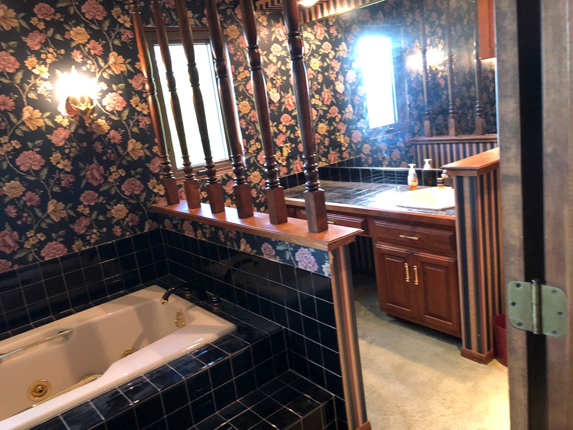 A bathroom with a tub , sink , mirror and floral wallpaper.