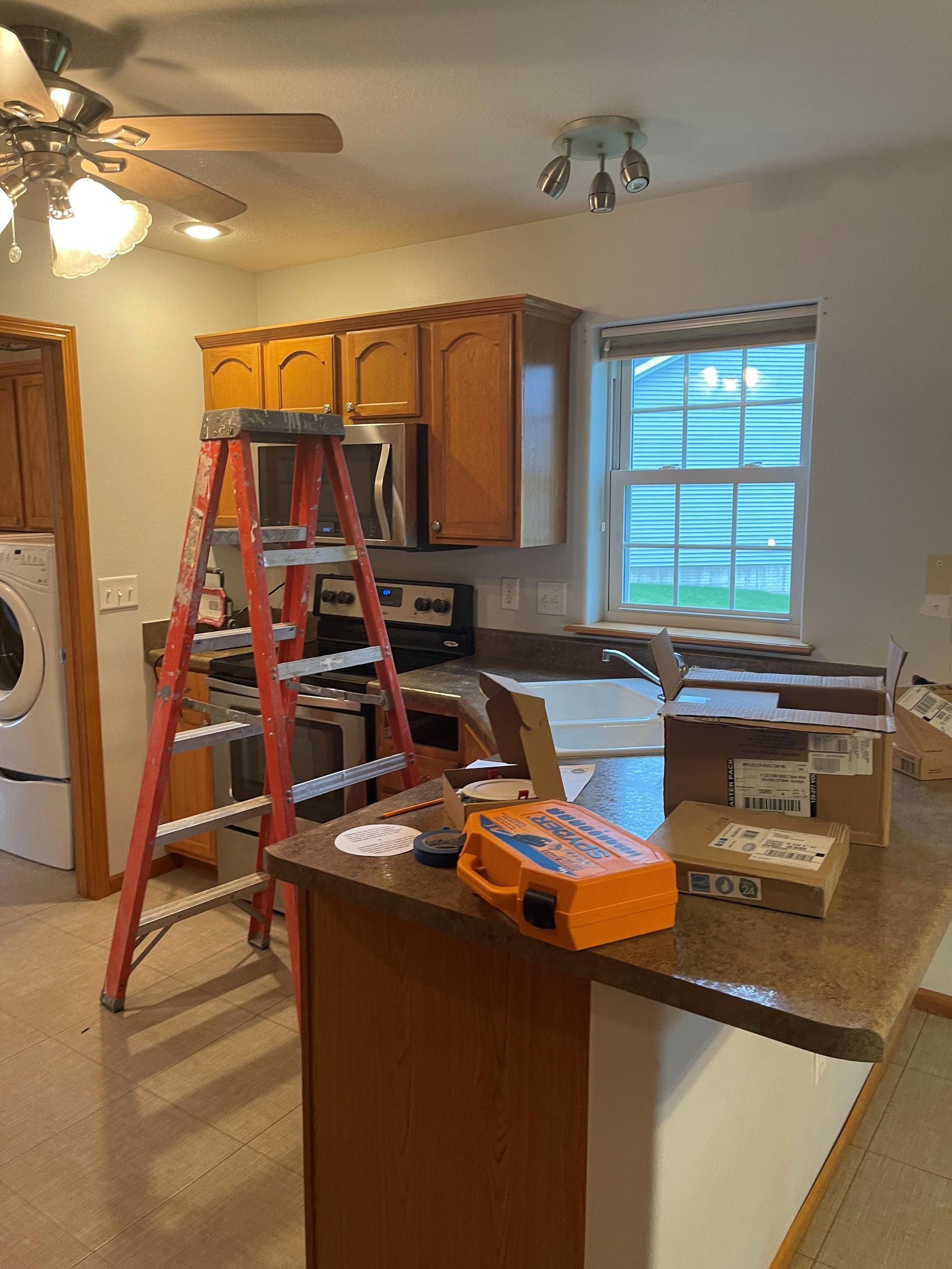 A kitchen with a ladder on the counter and a ceiling fan.