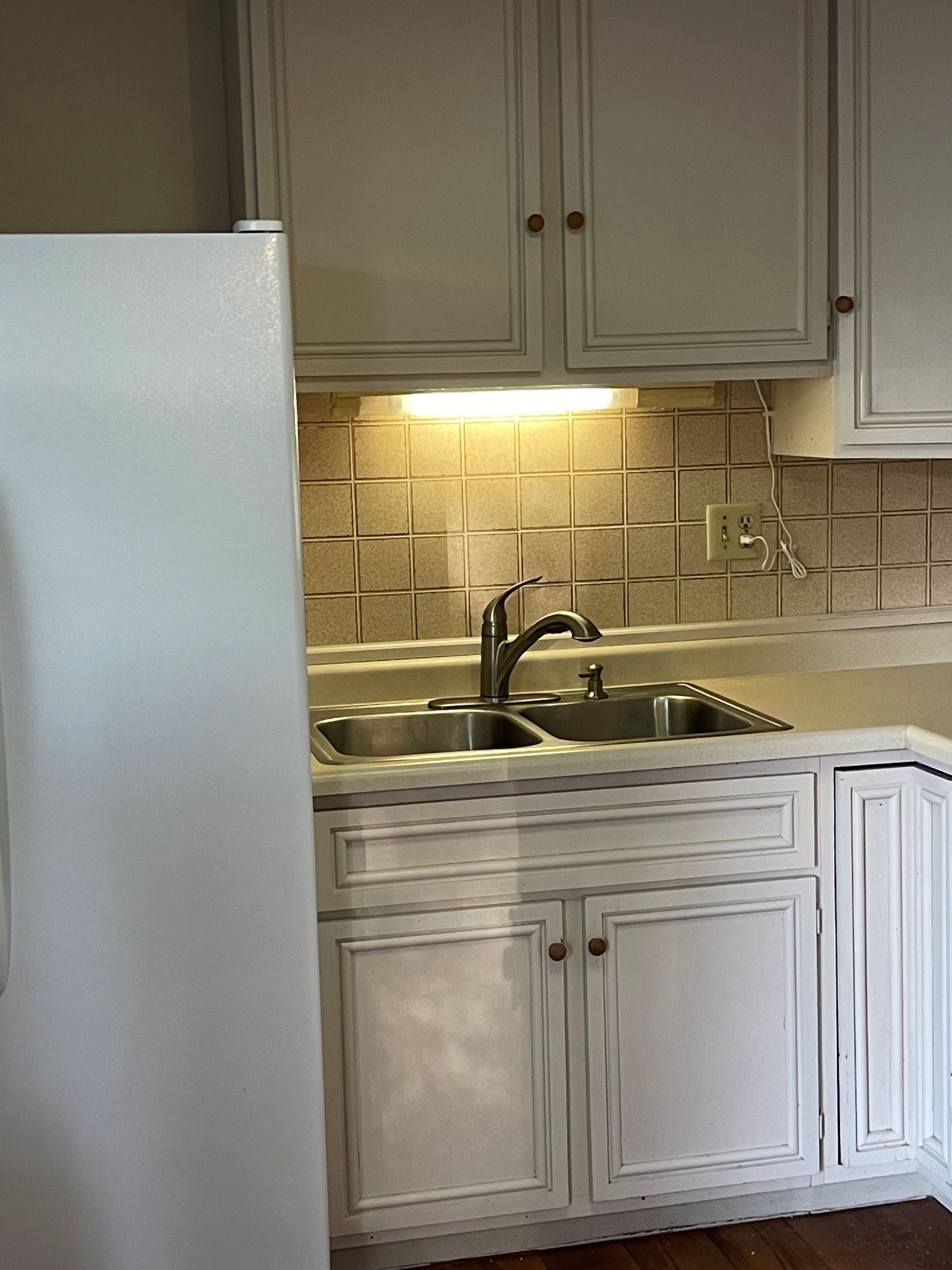 A kitchen with white cabinets a sink and a refrigerator