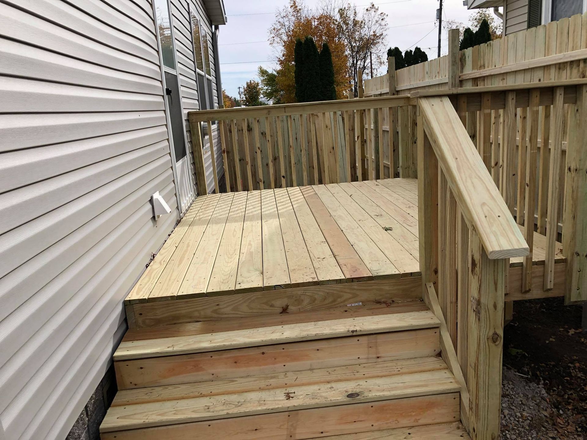 A wooden deck with stairs leading up to it next to a white house.