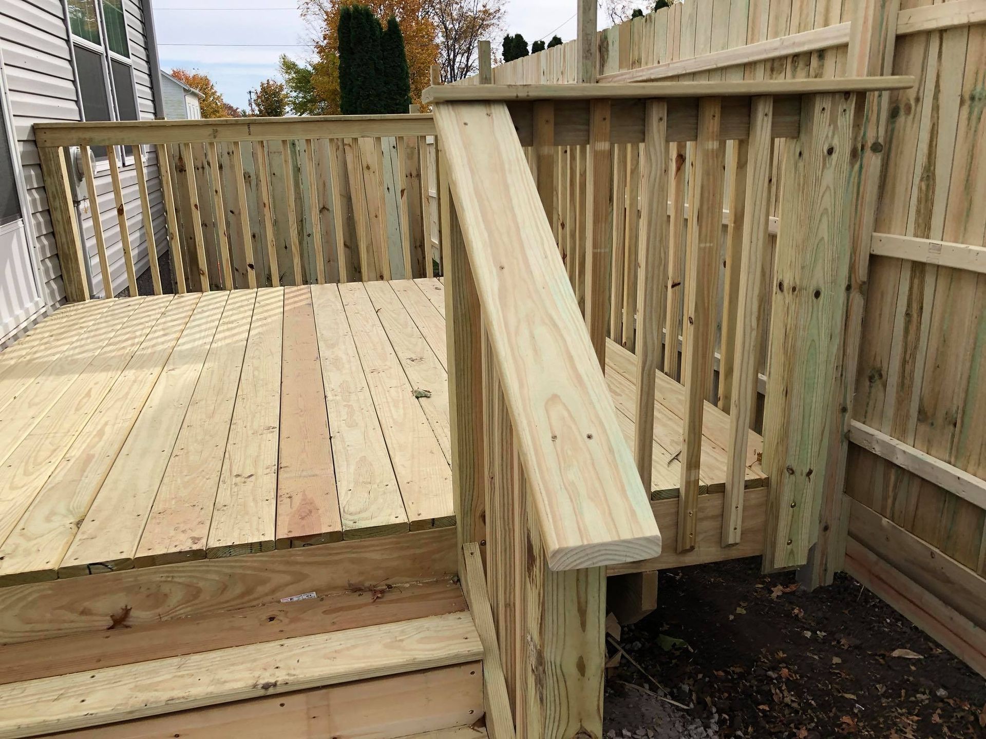 A wooden deck with stairs and a fence in the background.