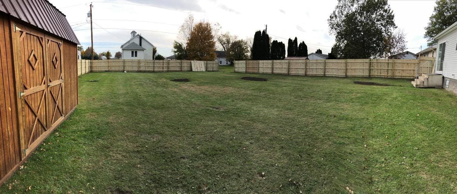 A large lawn with a wooden fence and a barn in the background.