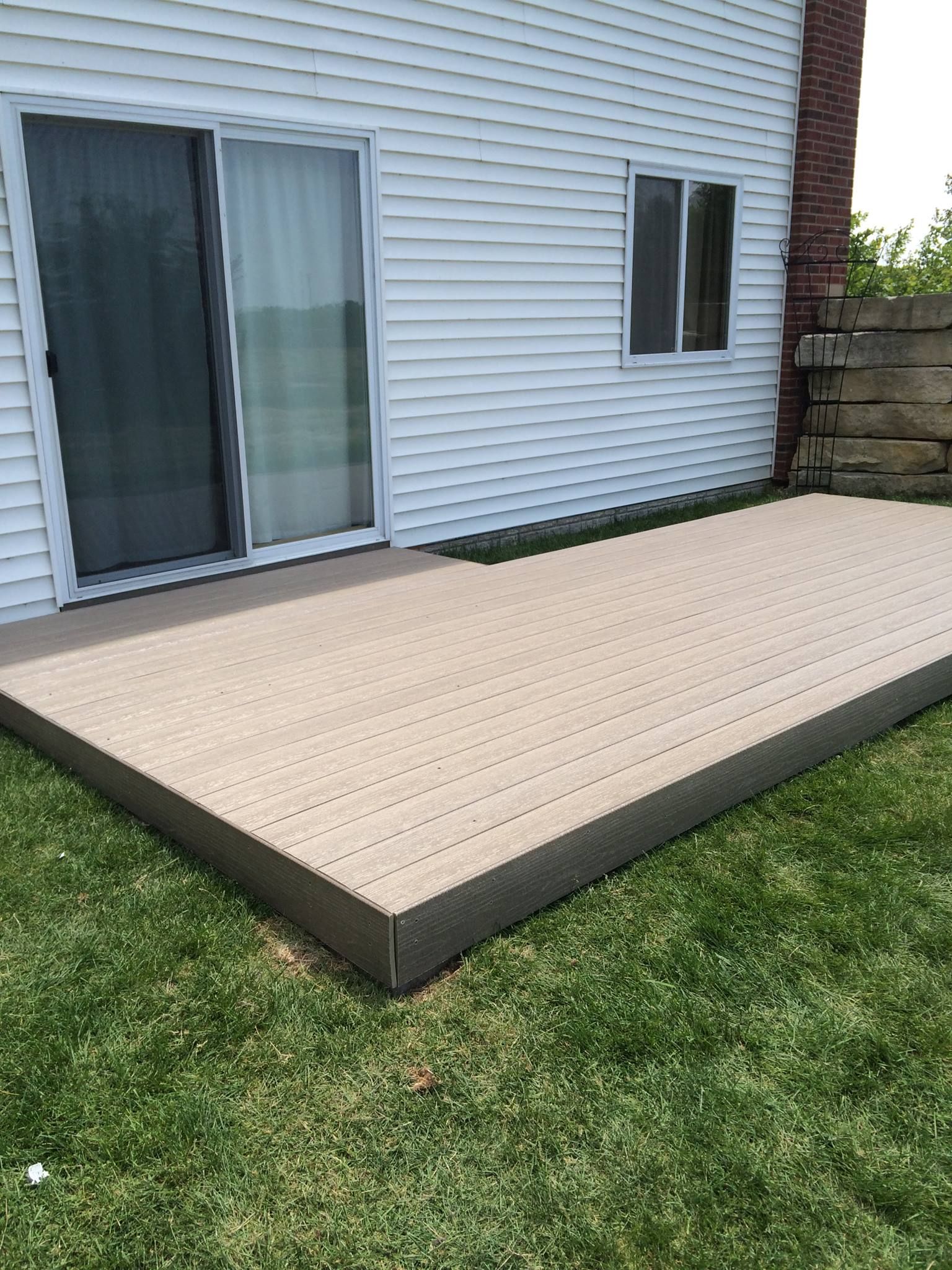 A deck is sitting in the grass in front of a house with a sliding glass door.