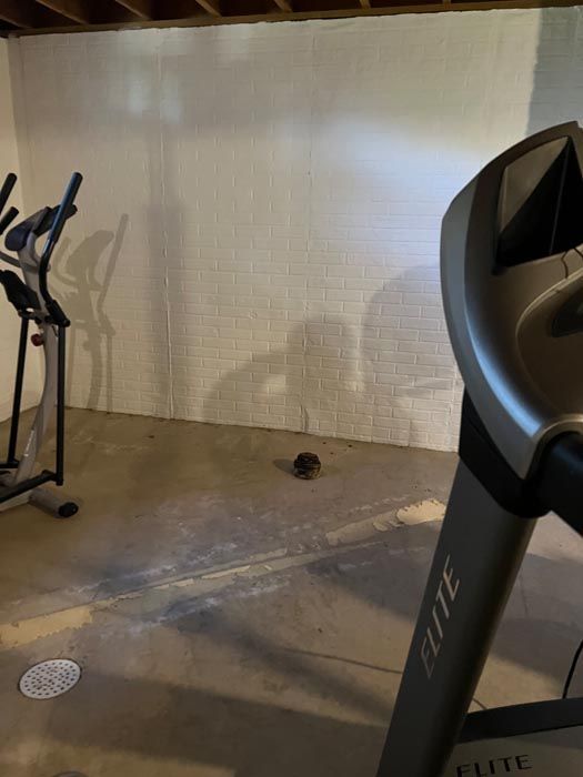 A treadmill and an elliptical are in a basement.