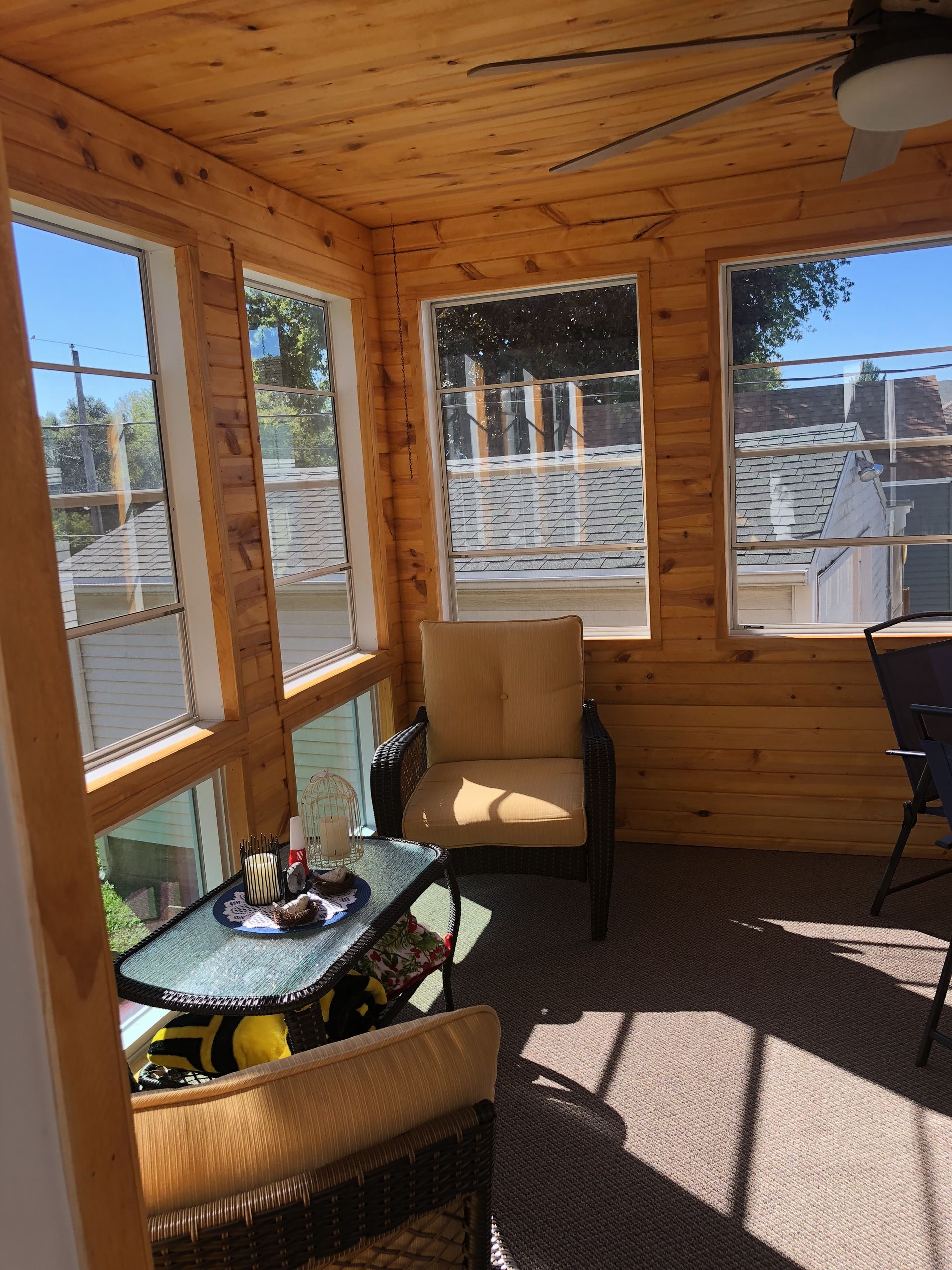 A screened in porch with a table and chairs and a ceiling fan.
