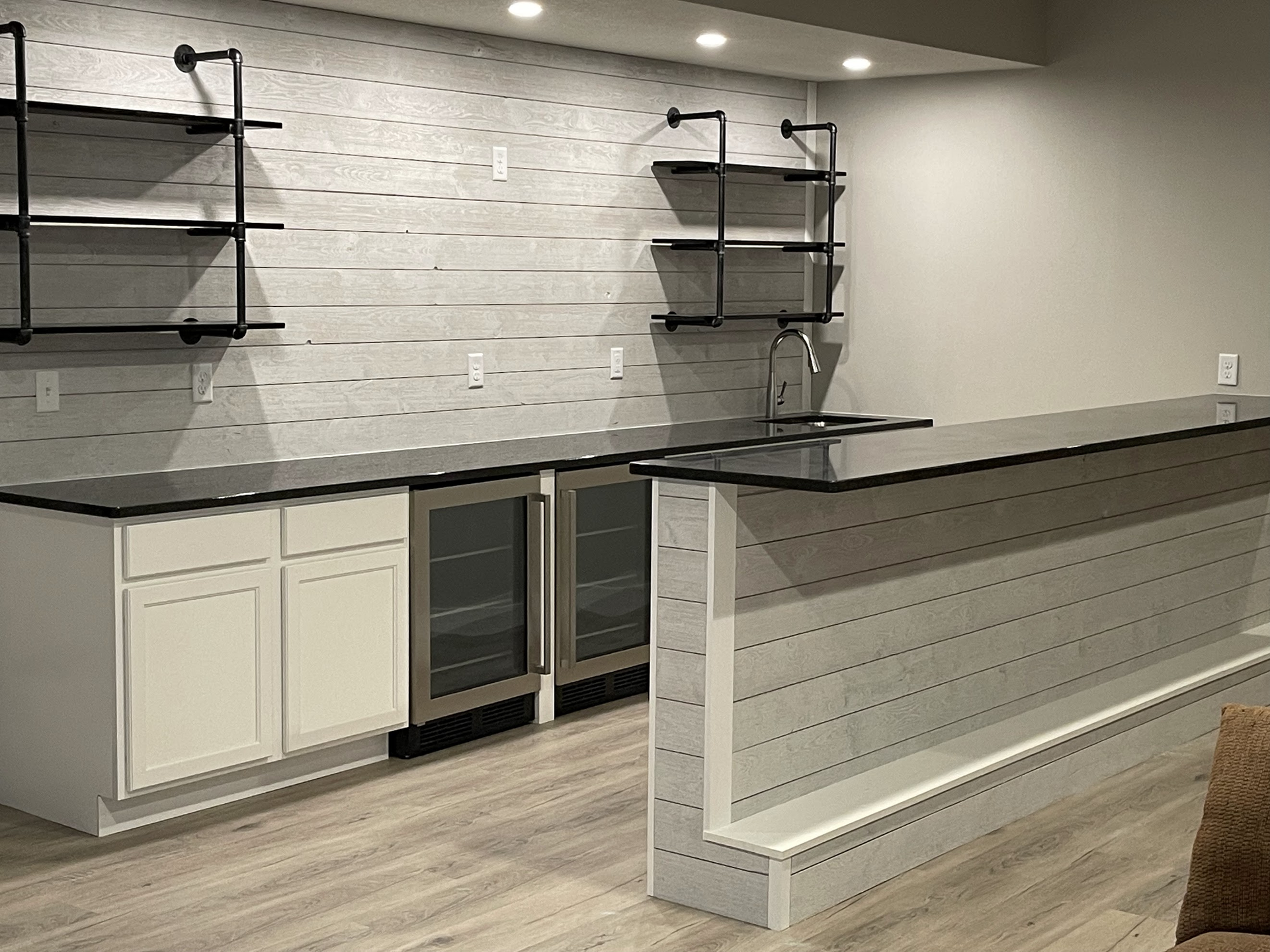 A kitchen with a bar , sink , refrigerator and shelves.