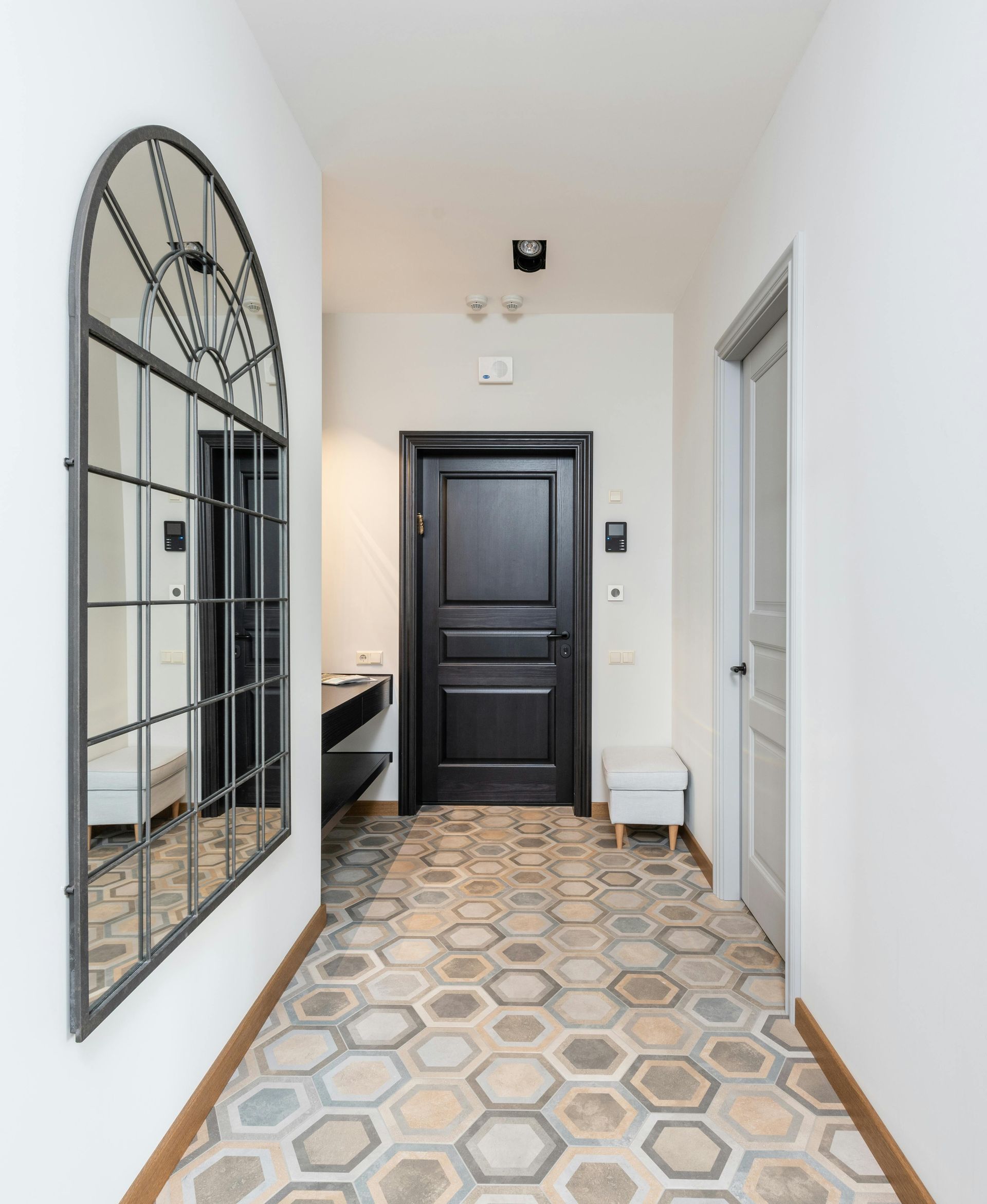A hallway with a black door and a mirror on the wall