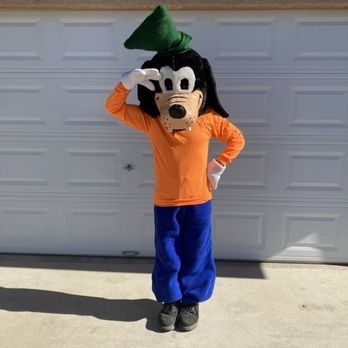 A person in a Goofy costume saluting in front of a white garage door.