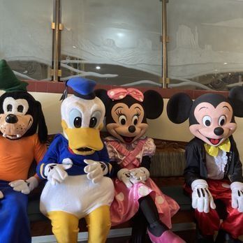 Goofy, Donald Duck, Minnie Mouse, and Mickey Mouse sit together; they are costumed characters.