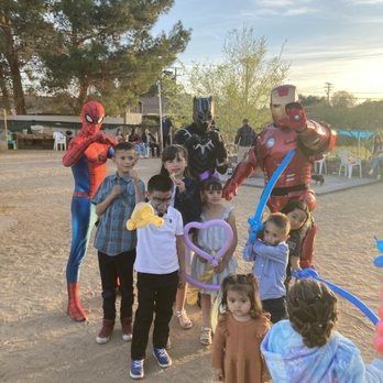 Spider-Man, Black Panther, Iron Man pose with children at an outdoor party.